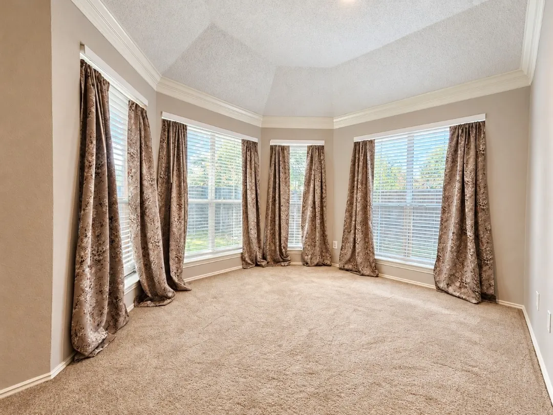 Expansive room with neutral carpeting, multiple windows with blinds and drapes, and a tray ceiling with crown molding
