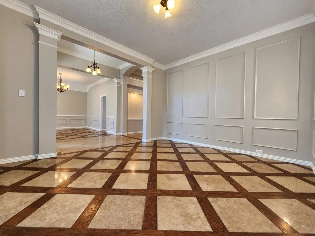 Expansive room featuring decorative wall paneling, crown molding, and a patterned tile and wood-finish flooring