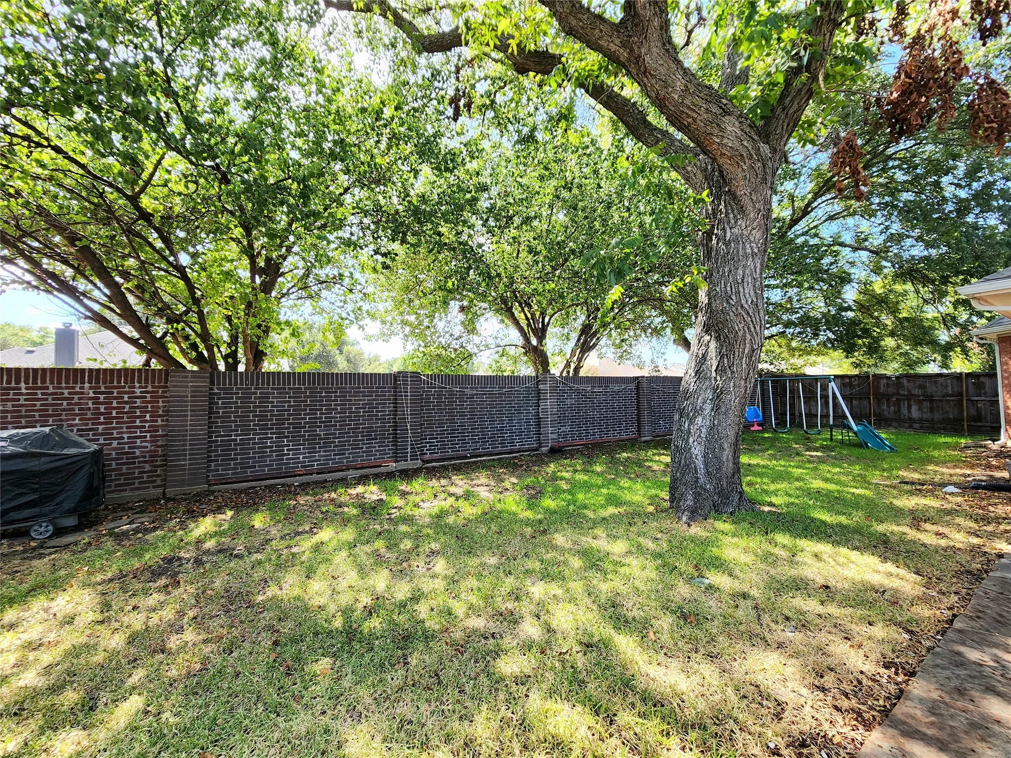 Expansive backyard featuring a mature tree, a brick privacy fence, and a grass lawn