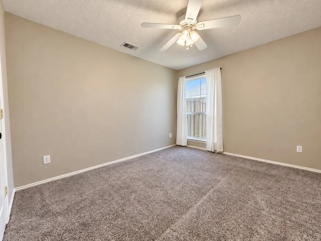 Carpeted room featuring neutral-toned walls, a window with vertical blinds, and a ceiling fan with integrated lighting
