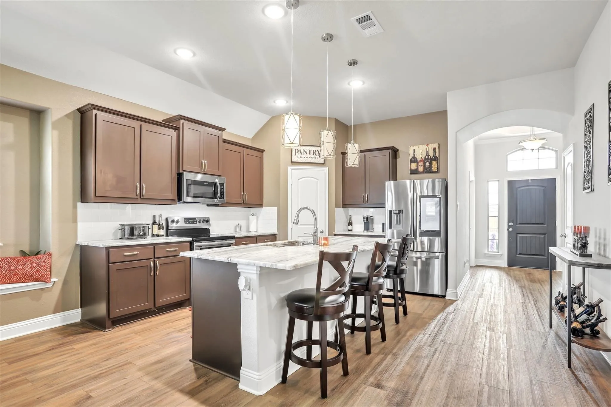 Kitchen featuring wood-finish flooring, dark wood cabinetry, white subway tile backsplash, and a center island with light-toned countertops
