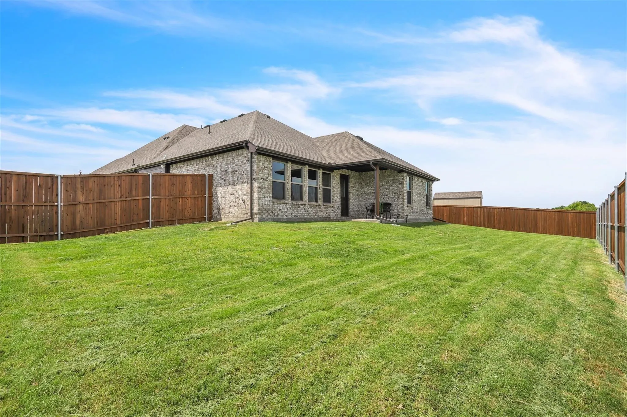 Expansive backyard with a manicured lawn, full privacy fencing, and a covered patio area