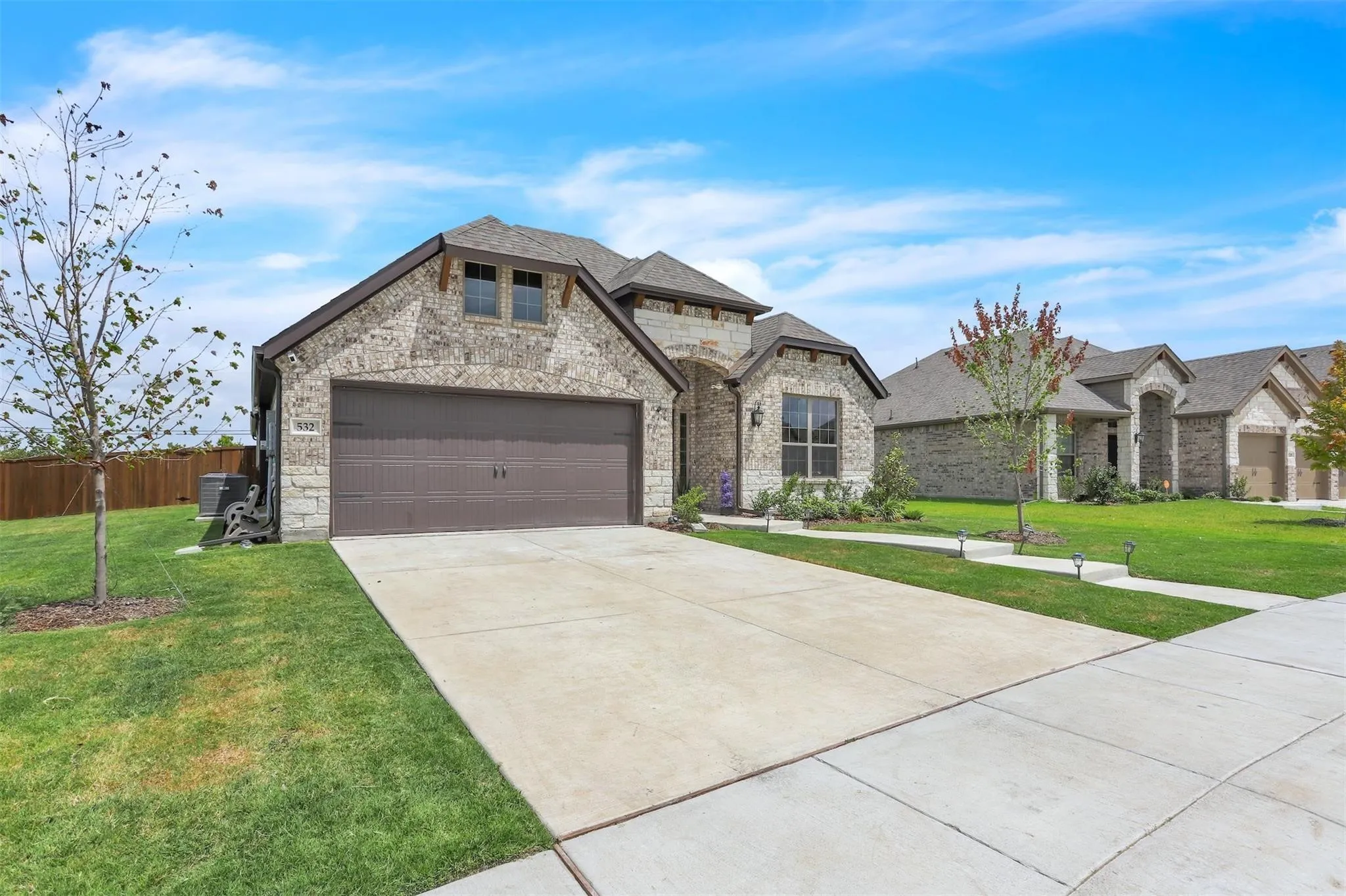 Stone and brick exterior with a two-car garage, concrete driveway, and front landscaping