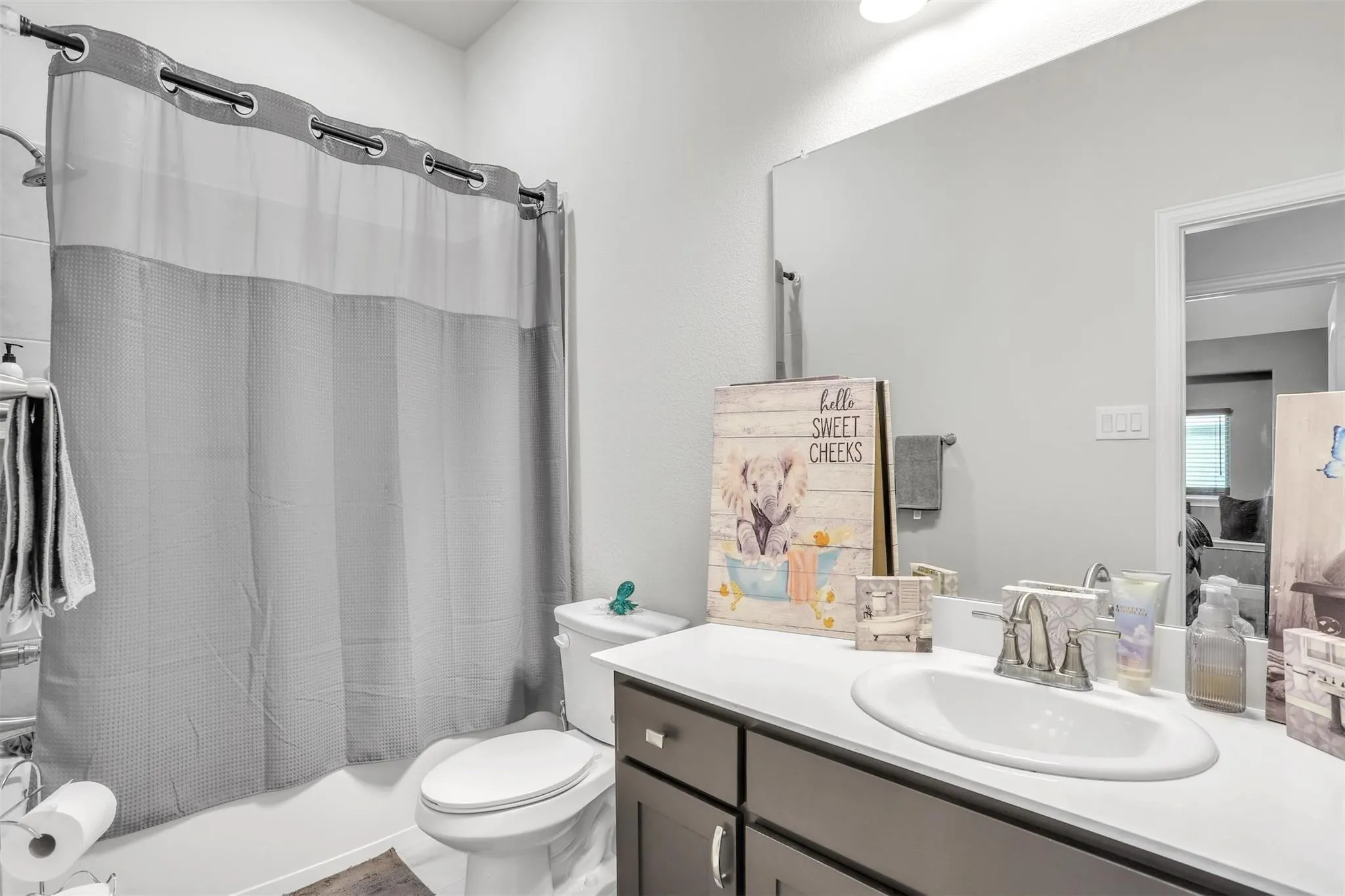 Bathroom featuring a single vanity with an integrated sink, dark wood-finish cabinetry, a full-width wall mirror, and a built-in bathtub with shower