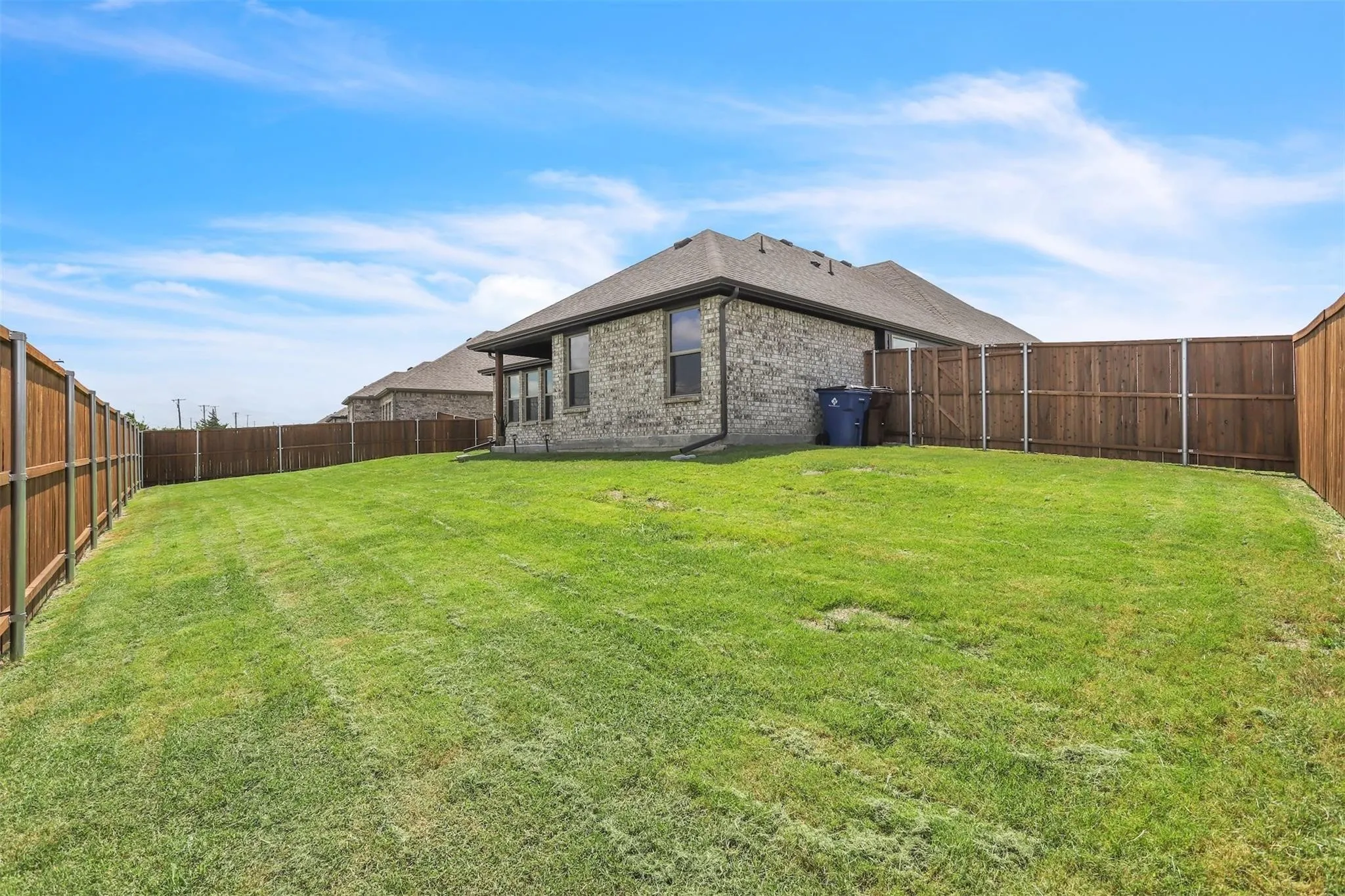 Expansive backyard featuring a green lawn, wood privacy fencing, and a brick exterior with multiple windows