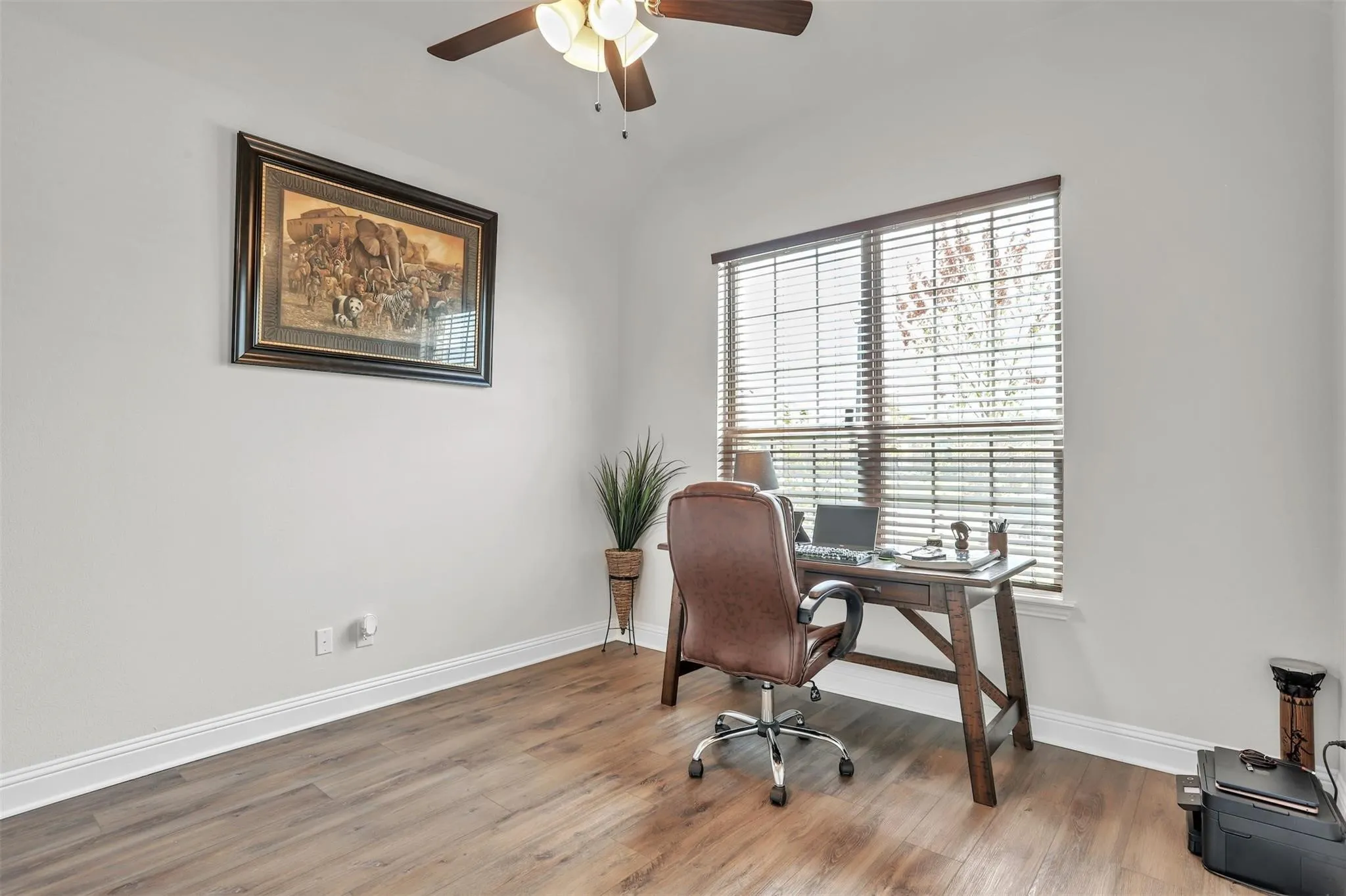 Spacious room featuring wood-finish flooring, a ceiling fan, and a large window with blinds