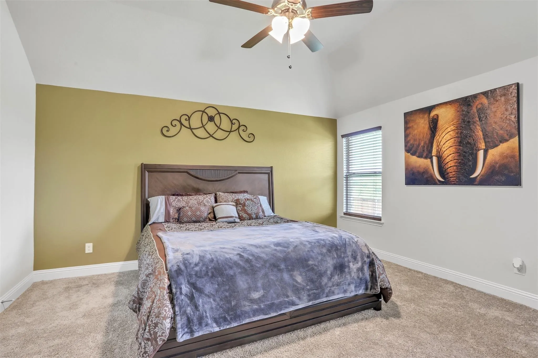 Vaulted ceiling with a ceiling fan, carpet flooring, a single window with horizontal blinds, and a contrasting accent wall