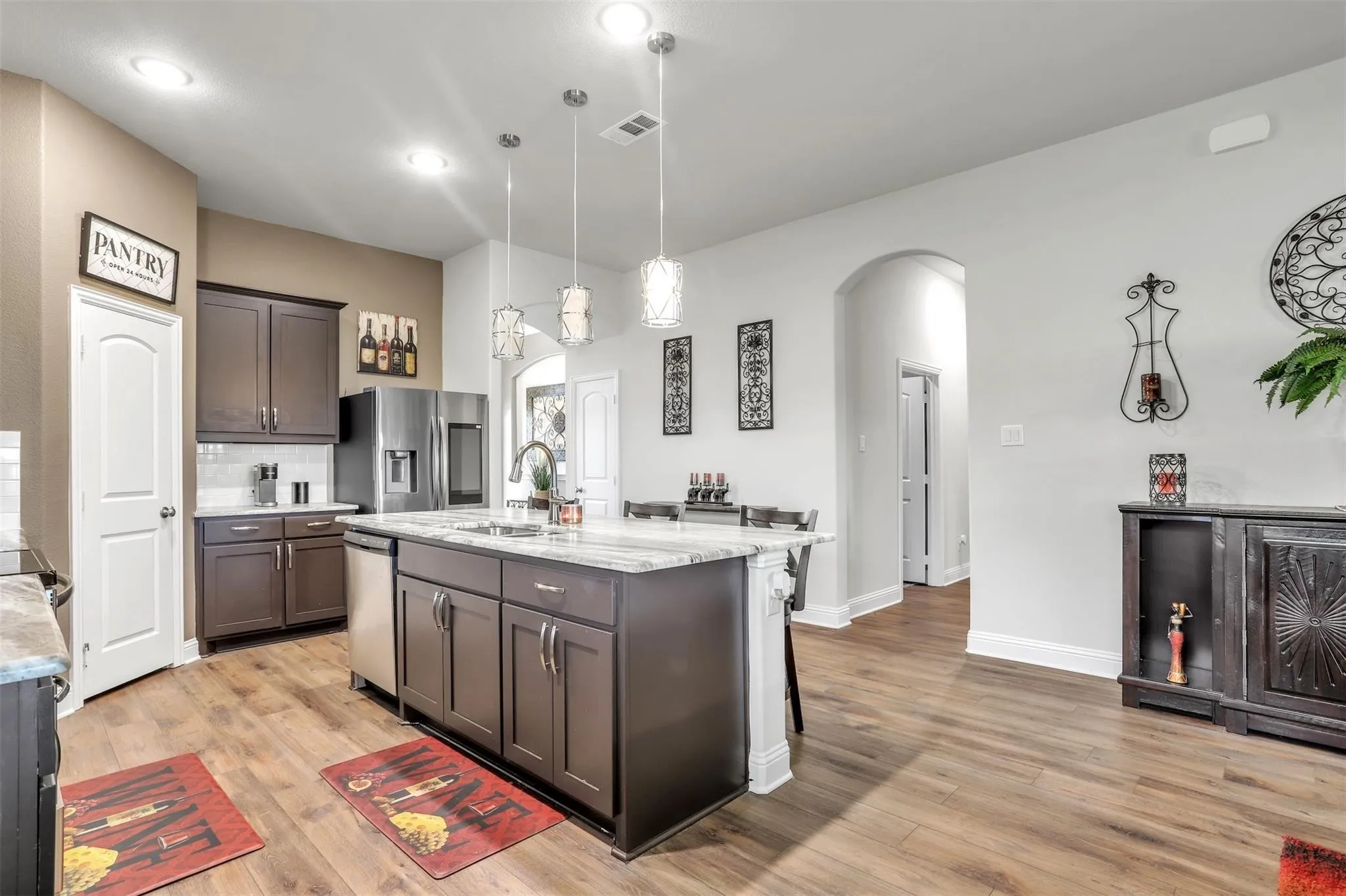 Kitchen featuring wood-finish flooring, dark wood cabinetry, stainless steel appliances, a center island with pendant lighting, and an arched doorway