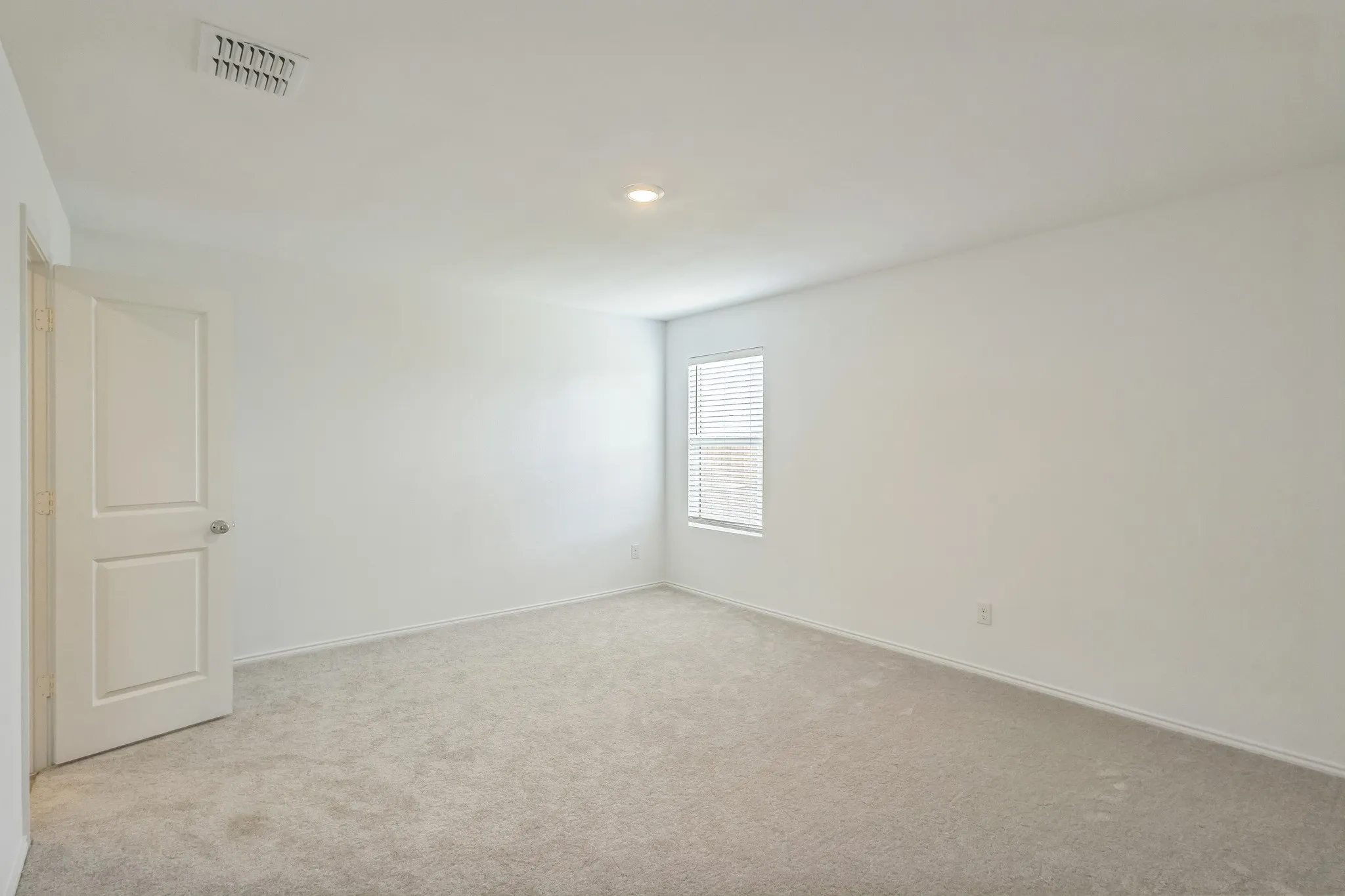 Spacious room featuring light-colored carpeting, a single window with blinds, and a white interior door