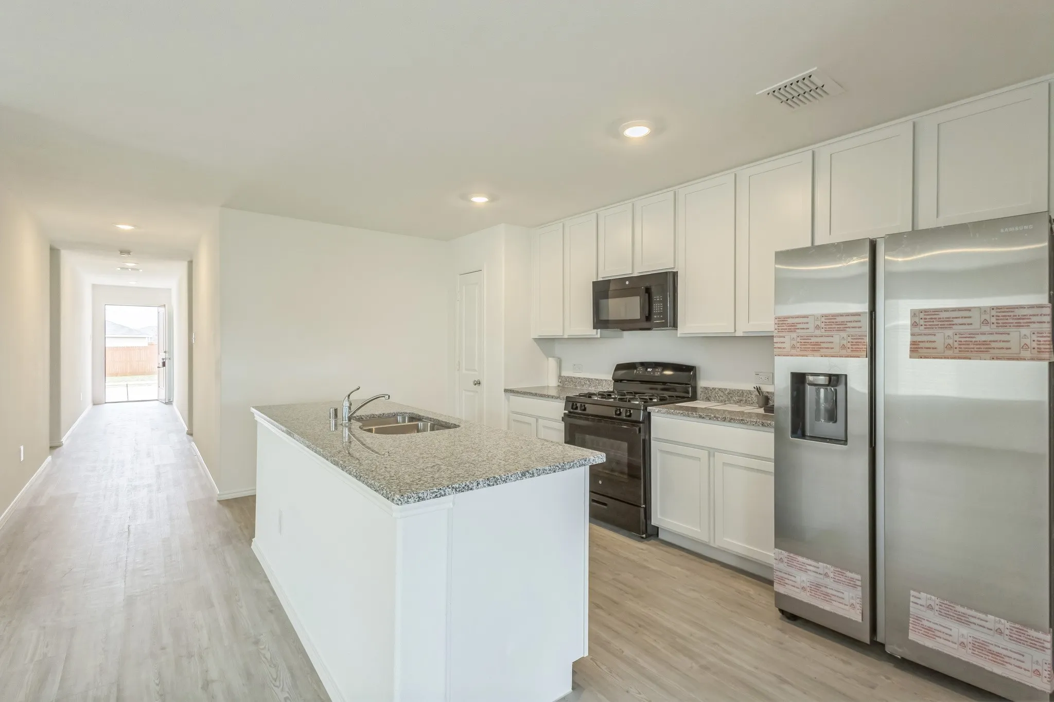 Kitchen featuring white cabinetry, granite-style countertops, an island with an integrated sink, and stainless steel appliances