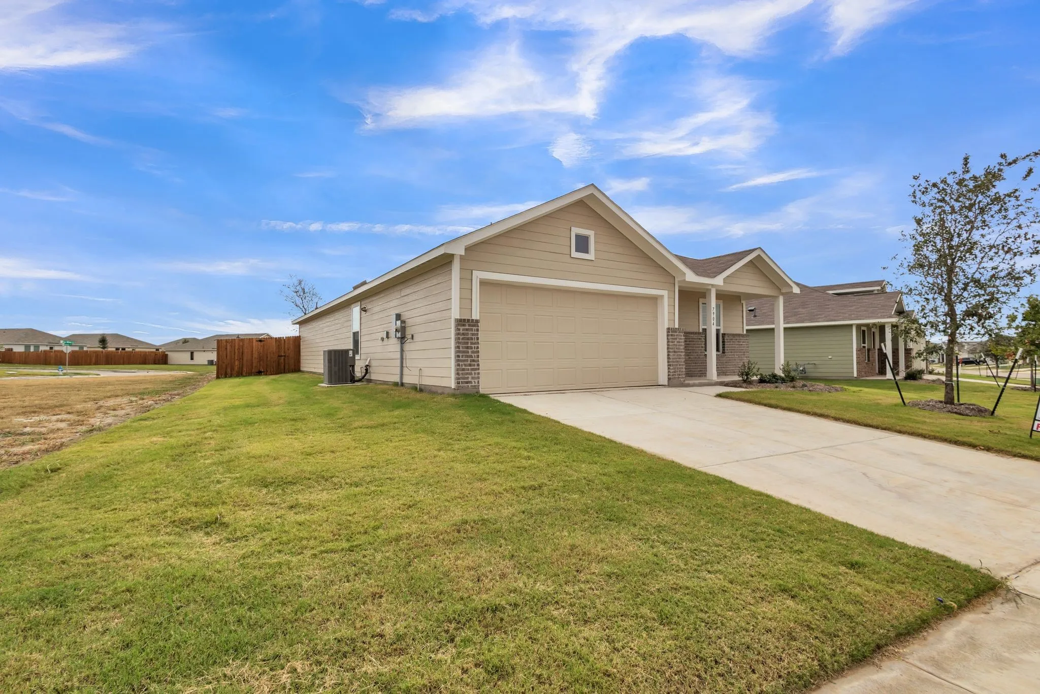 Single-story property featuring a tan exterior, an attached garage, a concrete driveway, and a manicured lawn