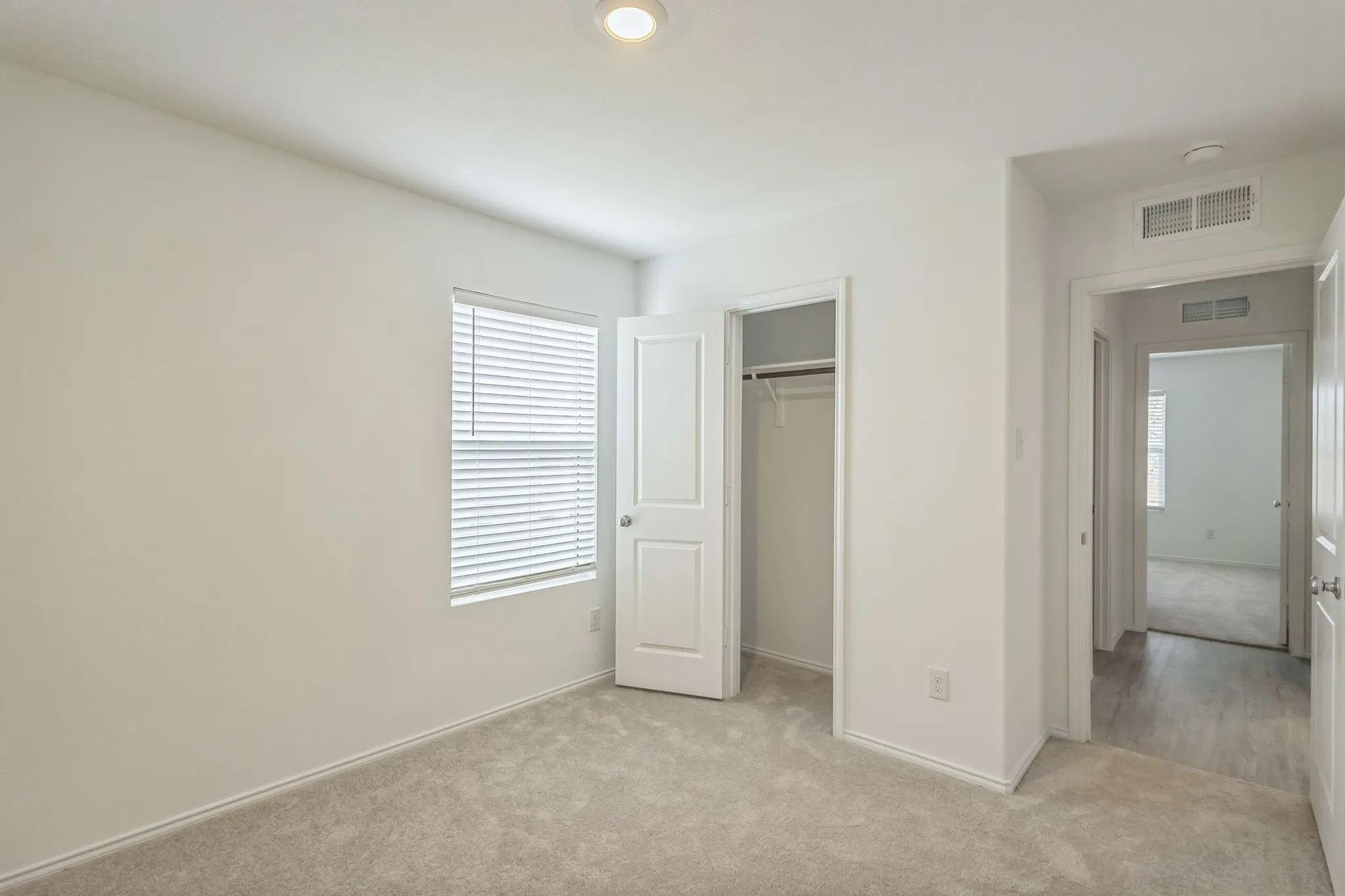 Carpeted room with a window, white blinds, and a built-in closet