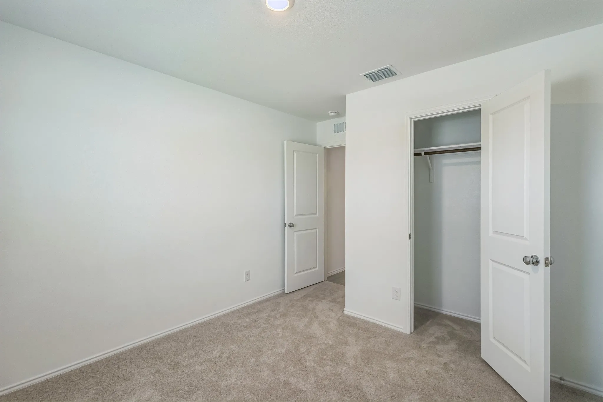 Recessed ceiling lighting, neutral carpeting, and a built-in closet with shelving and hanging rod