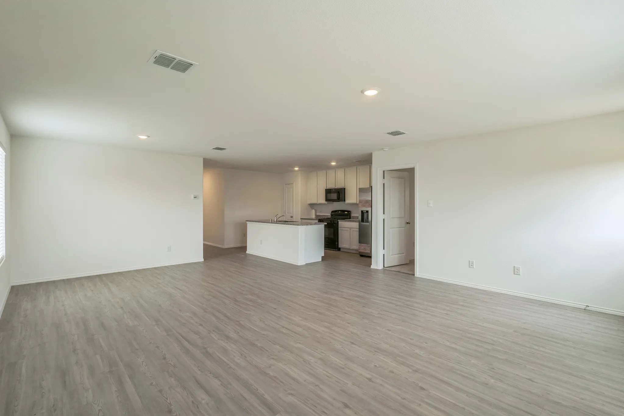 Open-concept living area featuring wood-finish flooring, recessed lighting, and a kitchen with an island, light-colored cabinetry, and black appliances
