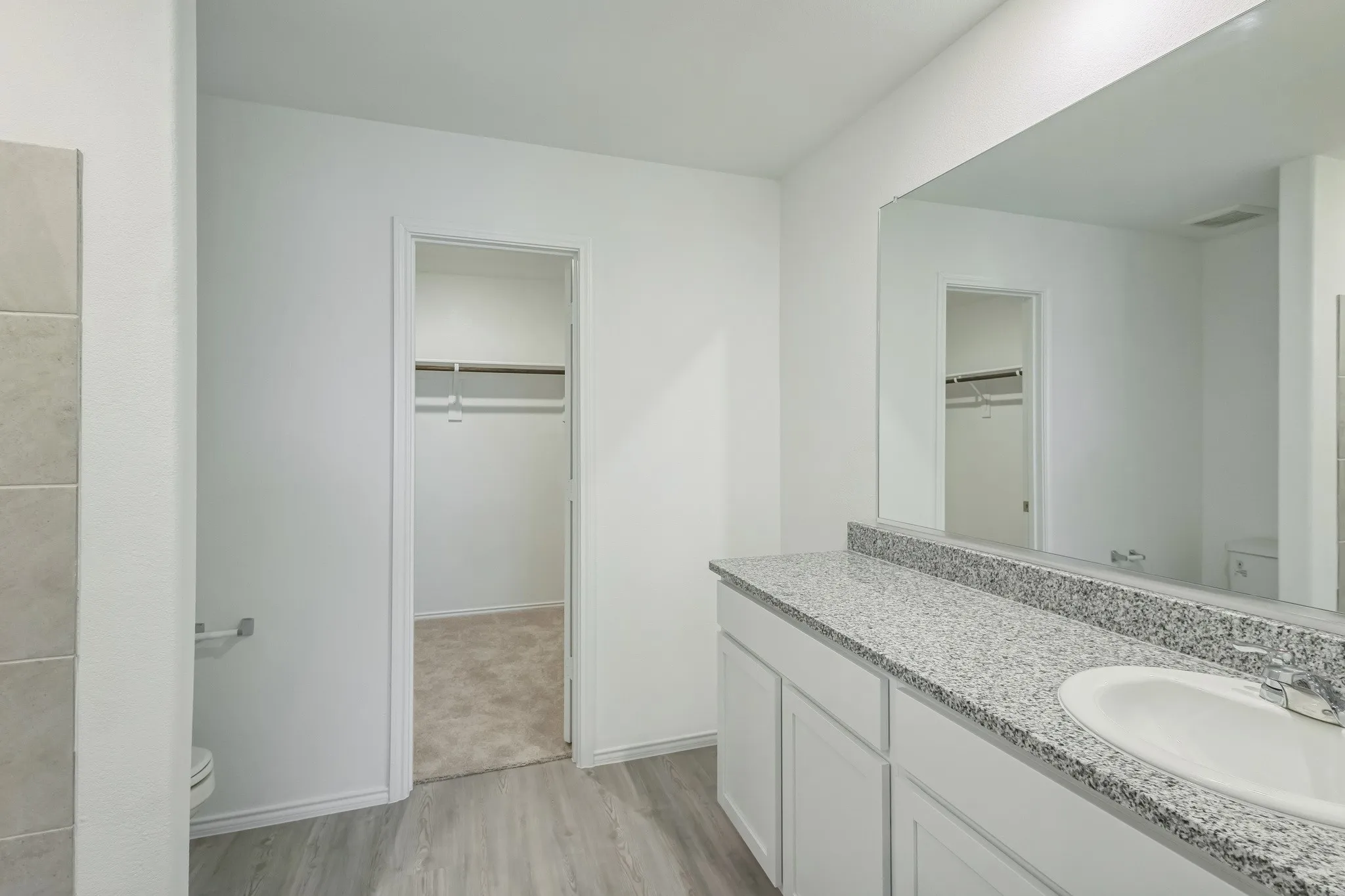 Wood-finish flooring, vanity with white cabinetry, integrated sink, and stone-finish countertop