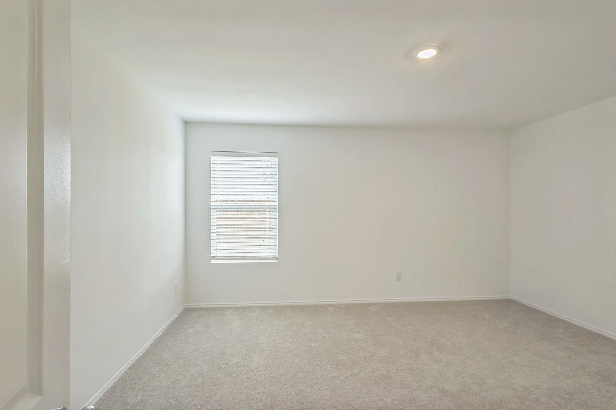 Neutral-toned carpeting, single window with horizontal blinds, recessed ceiling light, and white painted walls