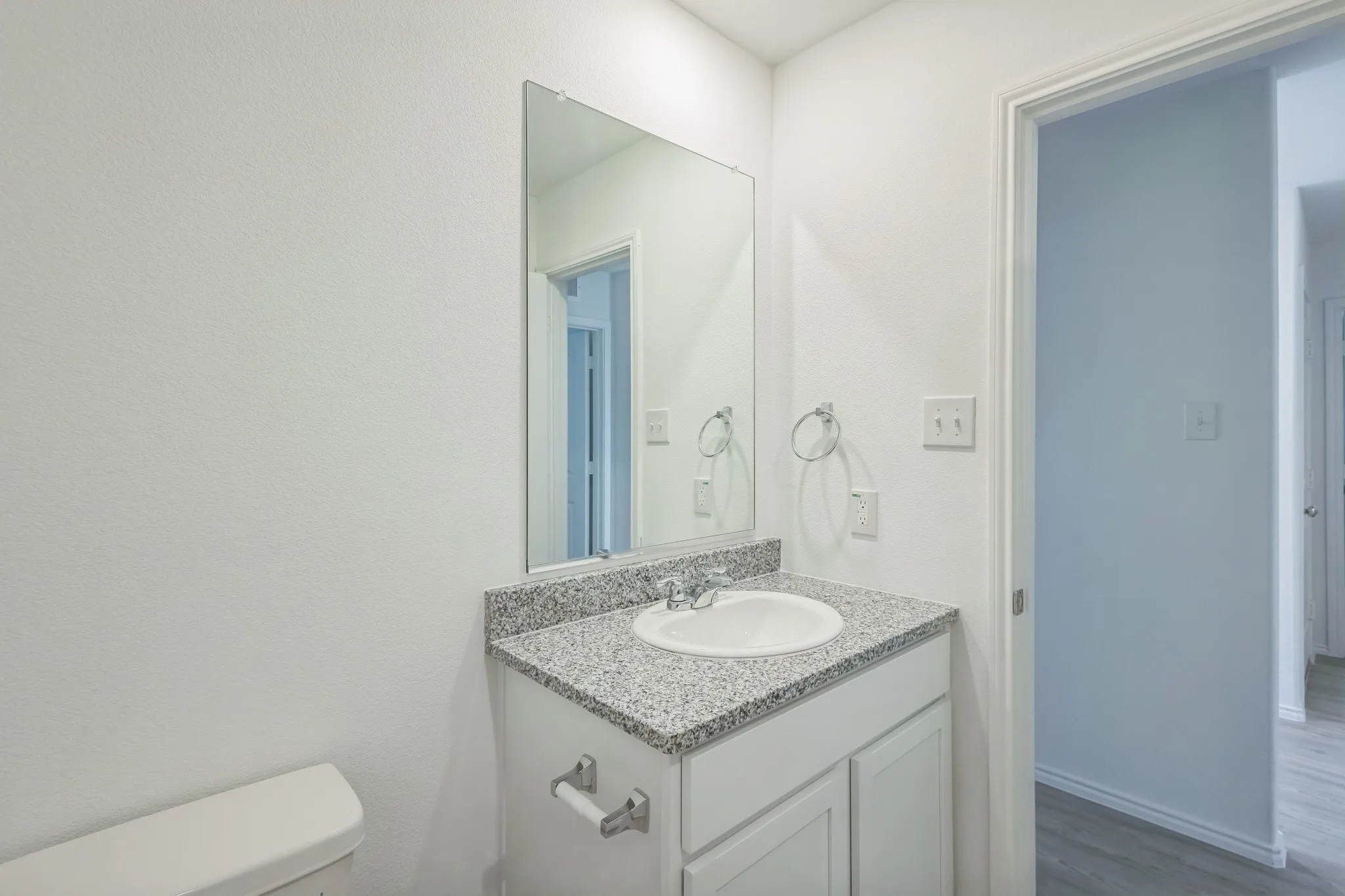 Bathroom featuring a vanity with a granular countertop, an integrated sink, a wall-mounted mirror, and a two-door cabinet