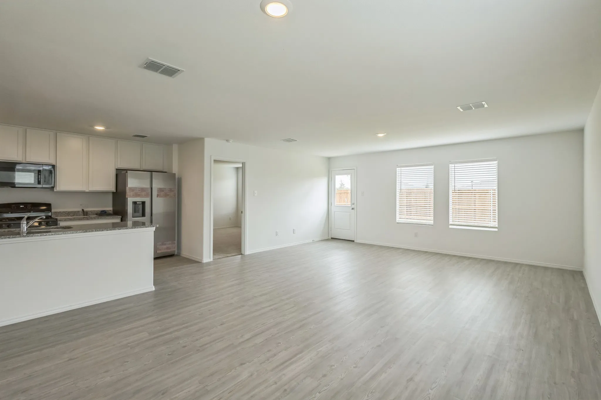 Open-concept kitchen and living area featuring wood-finish flooring, recessed lighting, white cabinetry, and stainless steel appliances