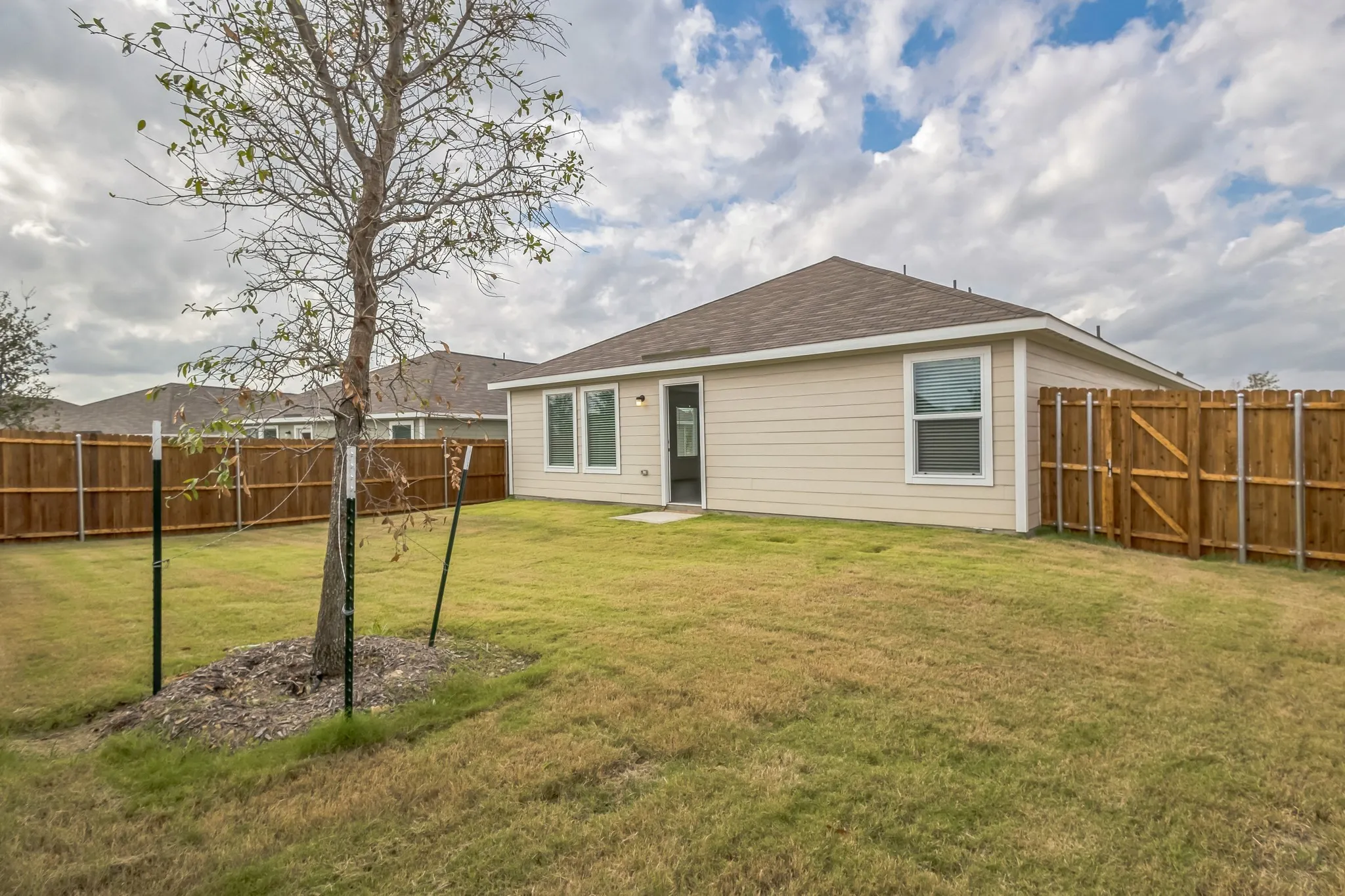 Expansive backyard featuring a mature tree, wood privacy fencing, and a light-colored siding exterior