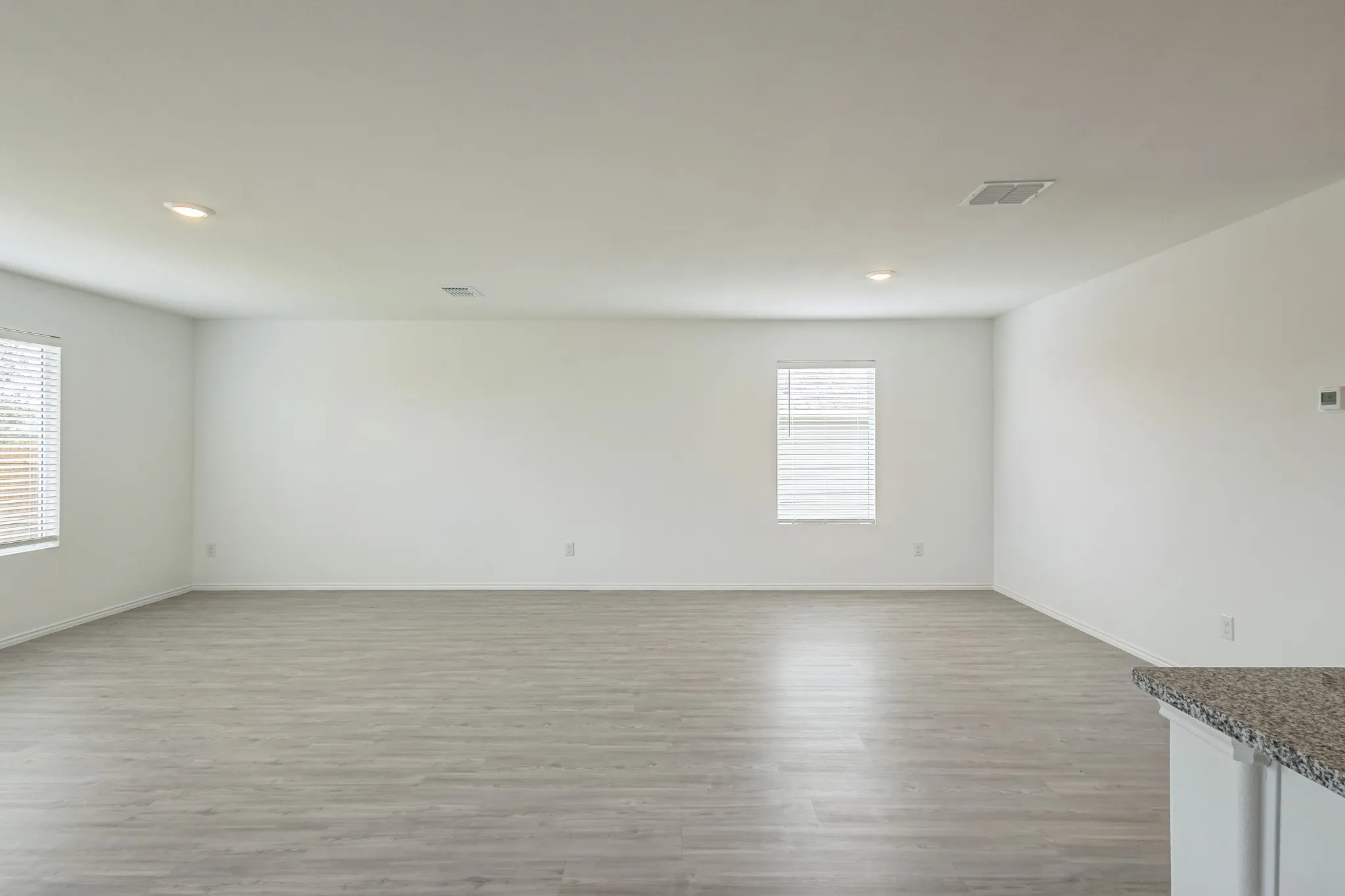 Spacious room with light wood-finish flooring, recessed lighting, multiple windows with blinds, and white walls