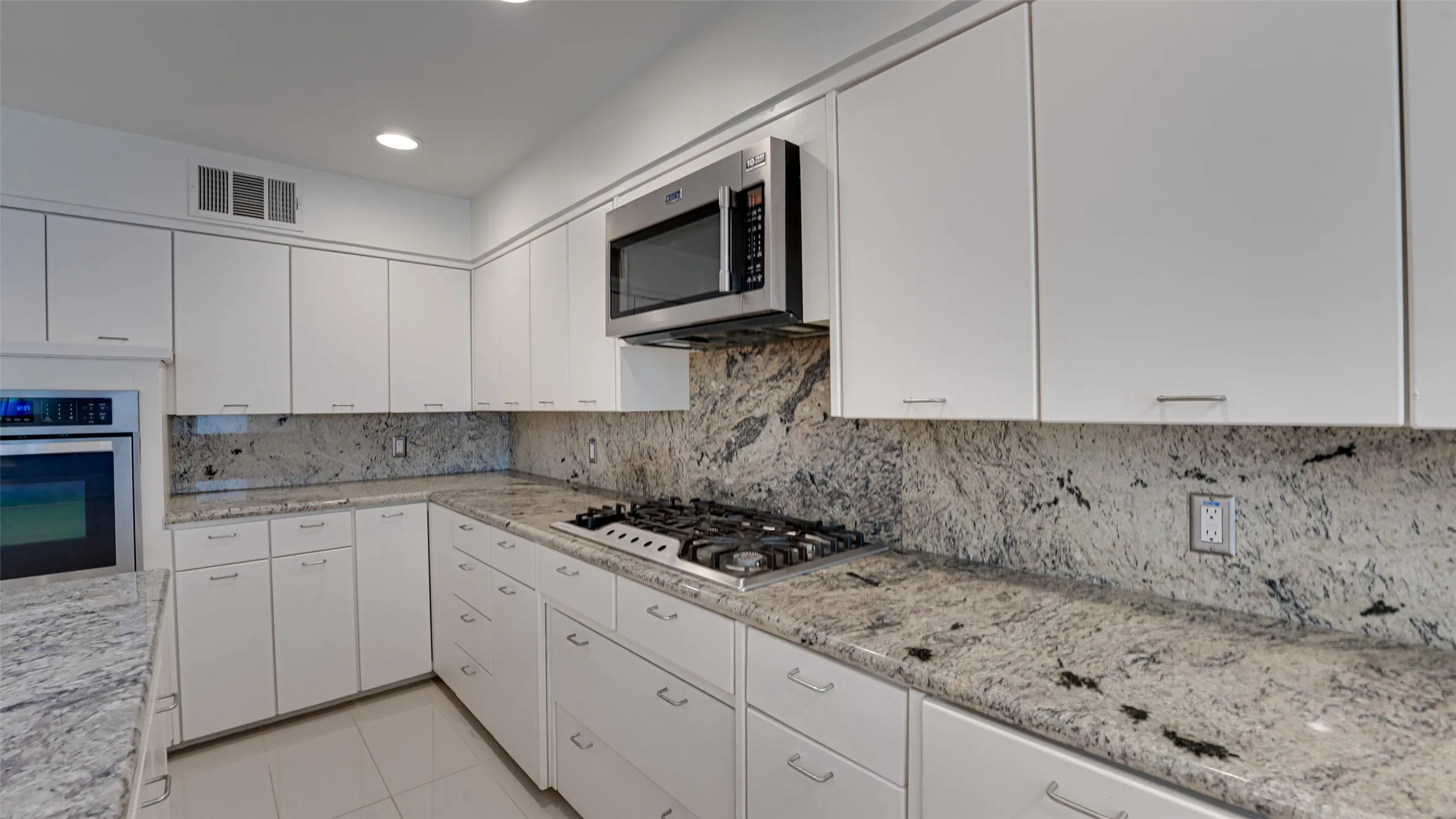 Kitchen with appliances with stainless steel finishes, white cabinets, light stone counters, light tile patterned floors, and decorative backsplash