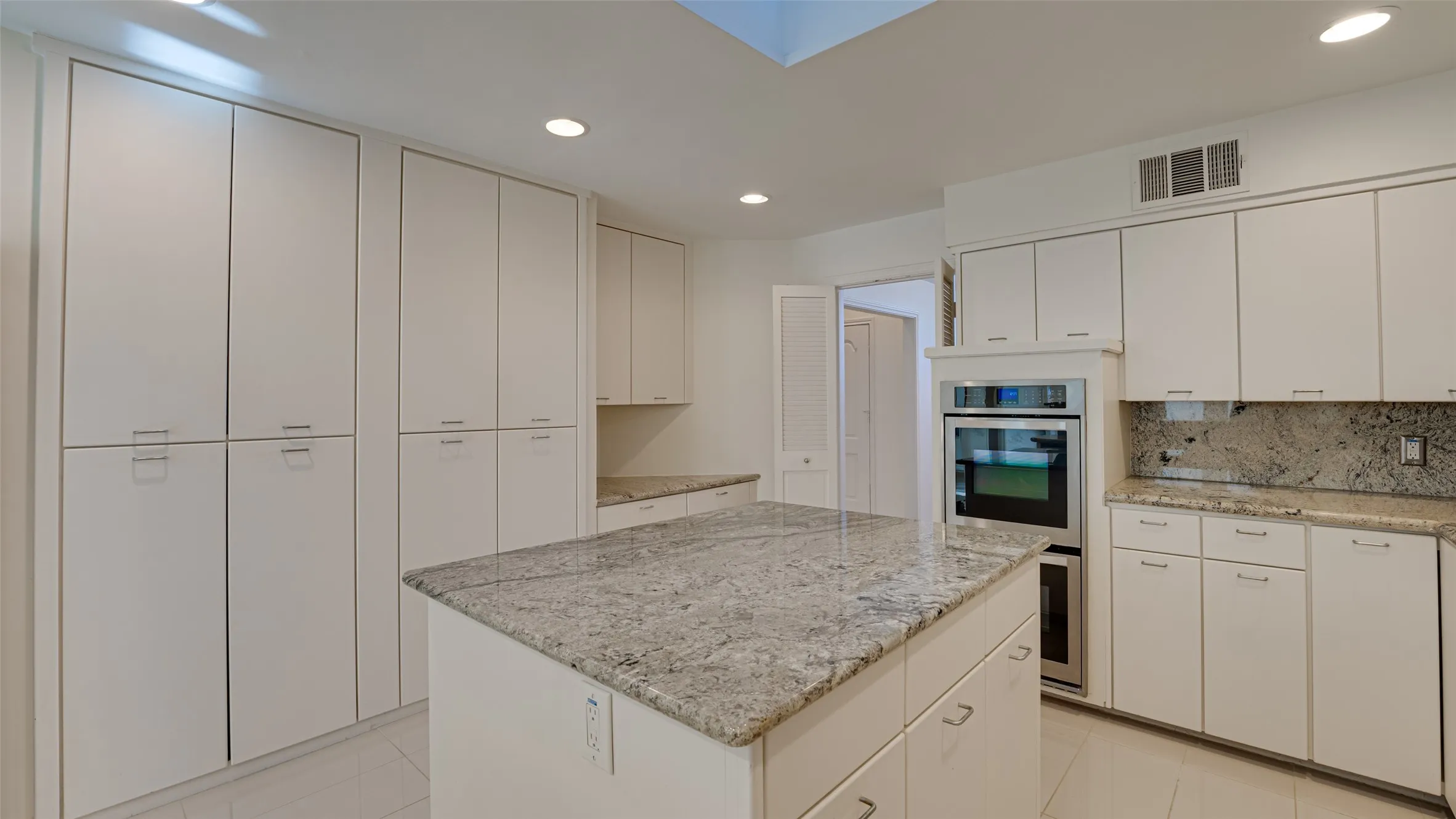 Kitchen featuring light tile patterned flooring, white cabinetry, decorative backsplash, a kitchen island, and double oven