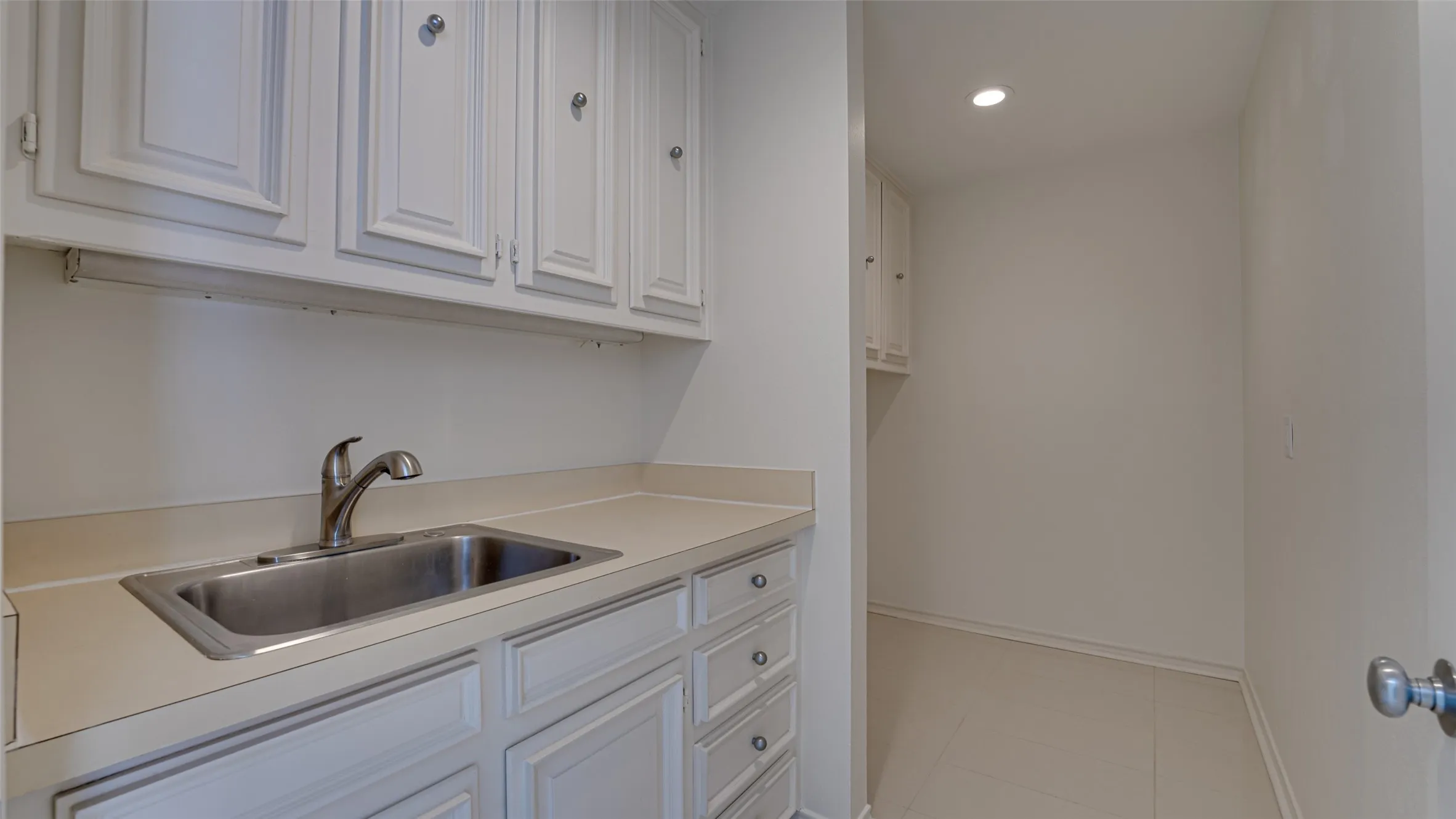 Laundry room featuring light tile patterned flooring, sink, and white cabinets