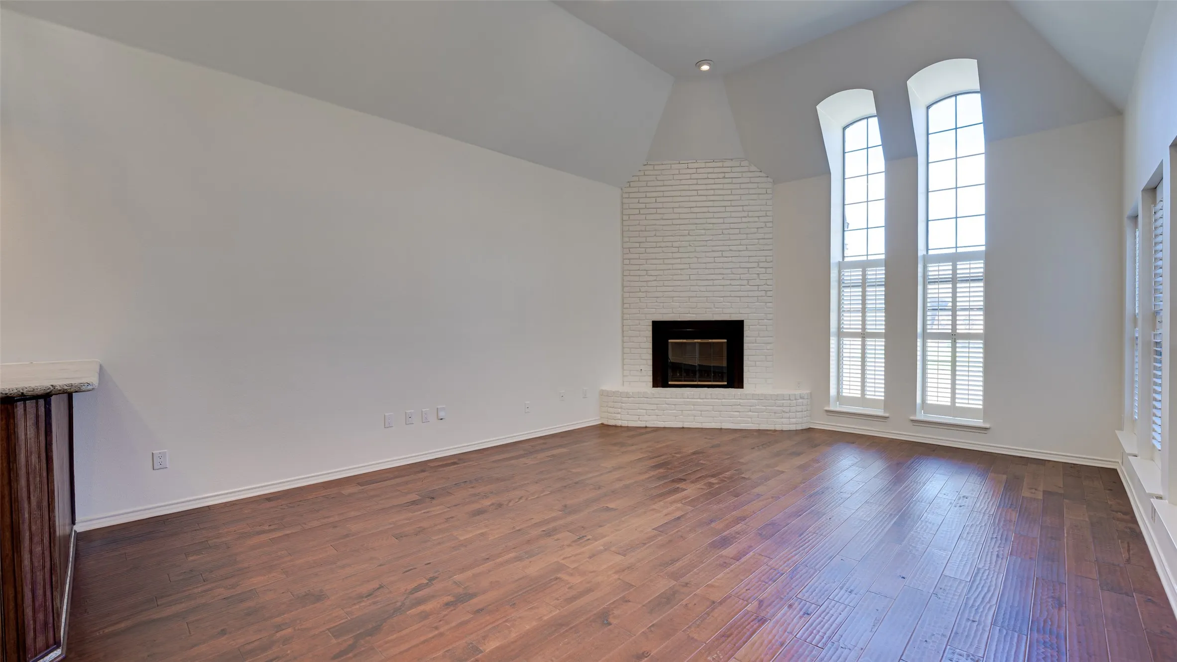 Unfurnished living room with high vaulted ceiling, brick wall, a brick fireplace, and hardwood / wood-style​​‌​​​​‌​​‌‌​‌‌​​​‌‌​‌​‌​‌​​​‌​​ floors