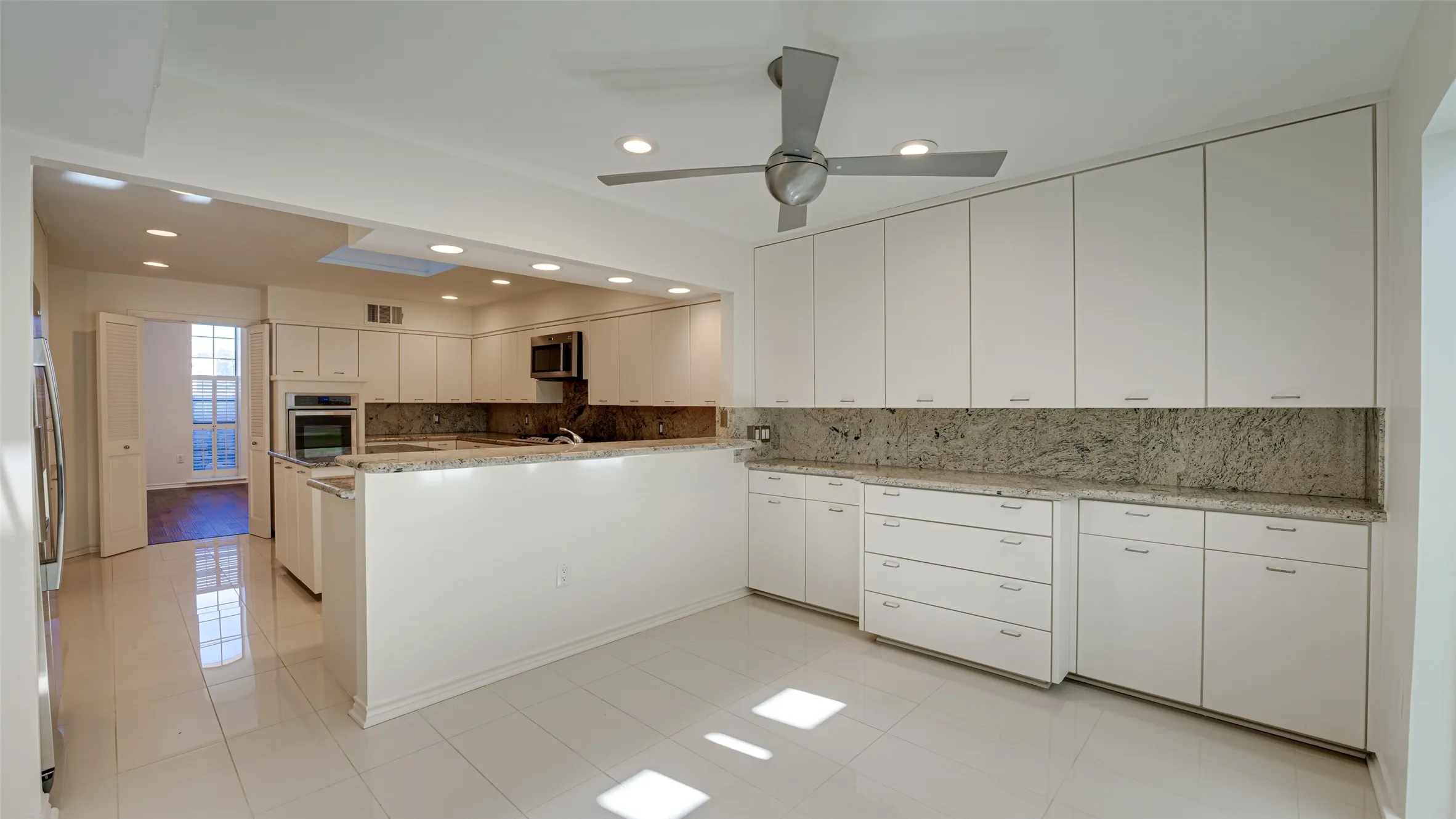 Kitchen featuring light tile patterned flooring, white cabinetry, kitchen peninsula, ceiling fan, and stainless steel appliances