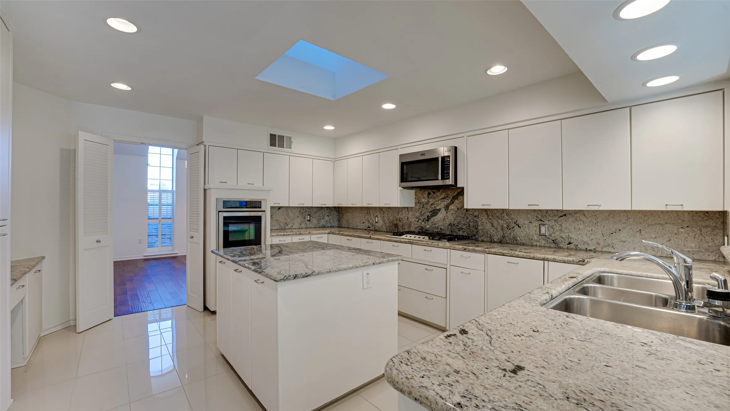 Kitchen with sink, double oven, white cabinets, stainless steel appliances, and light tile patterned floors