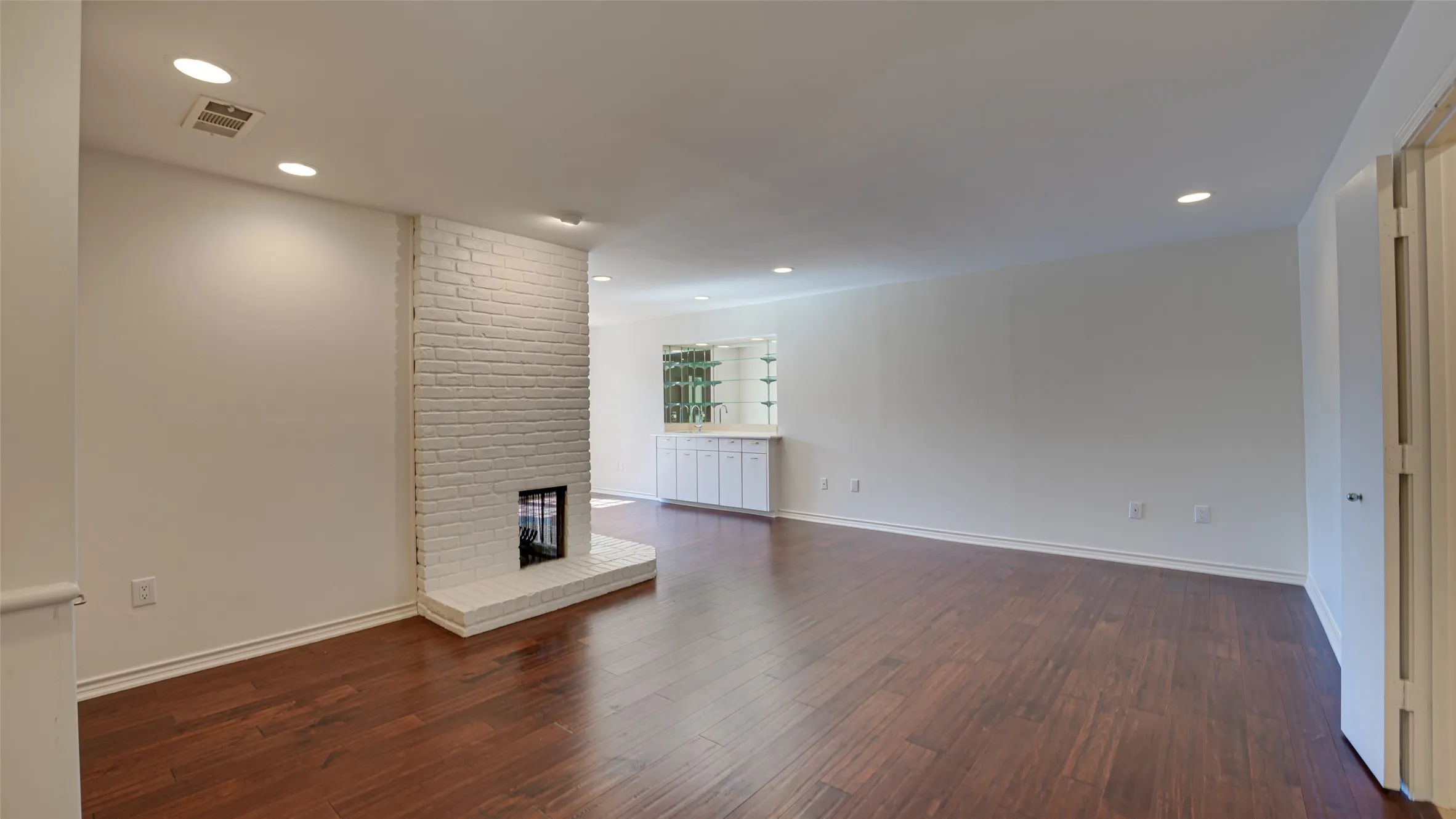 Primary bedroom featuring dark hardwood / wood-style floors, a brick fireplace, and brick wall