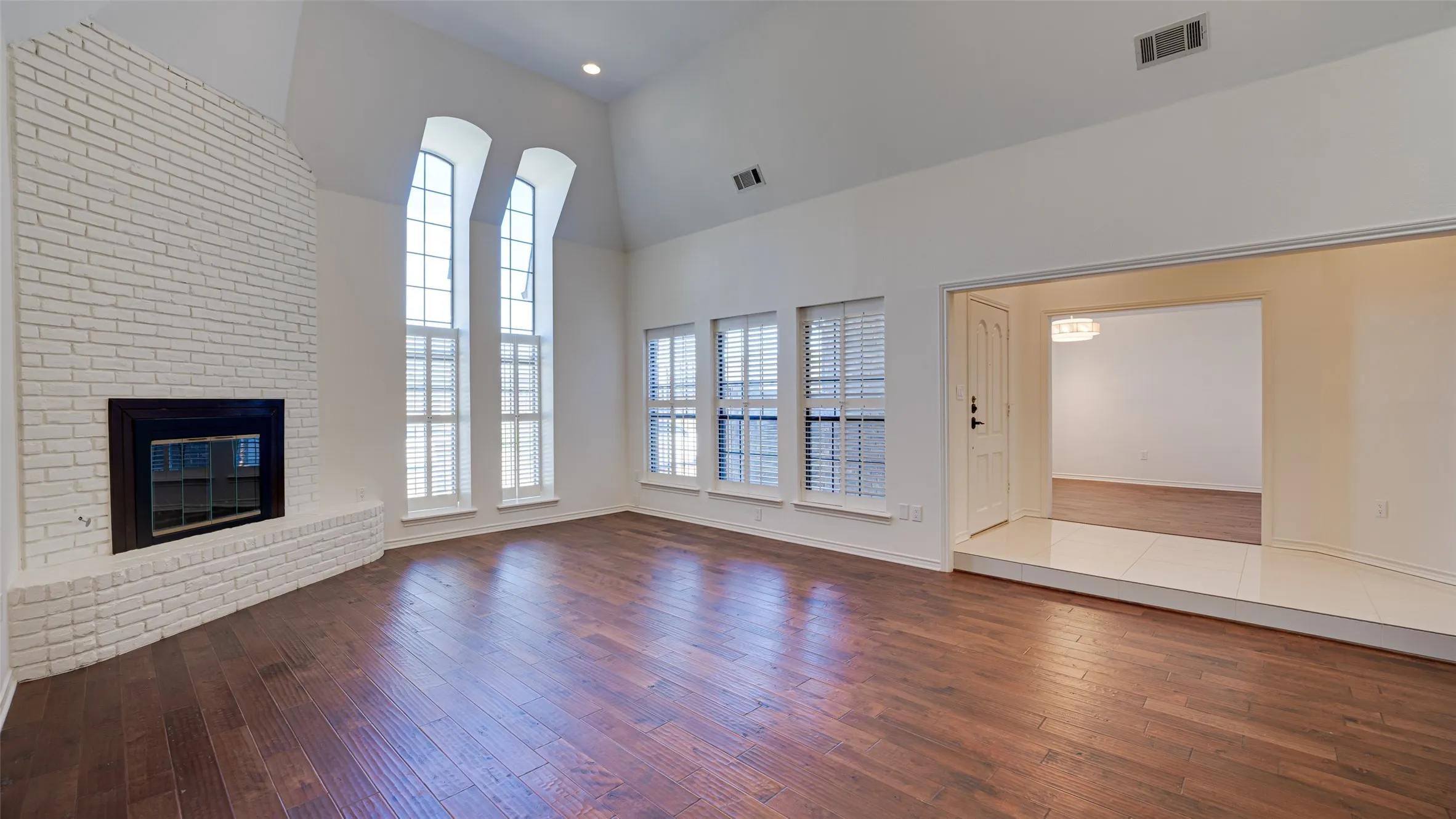 Unfurnished living room featuring hardwood / wood-style flooring, brick wall, a fireplace, and high vaulted ceiling