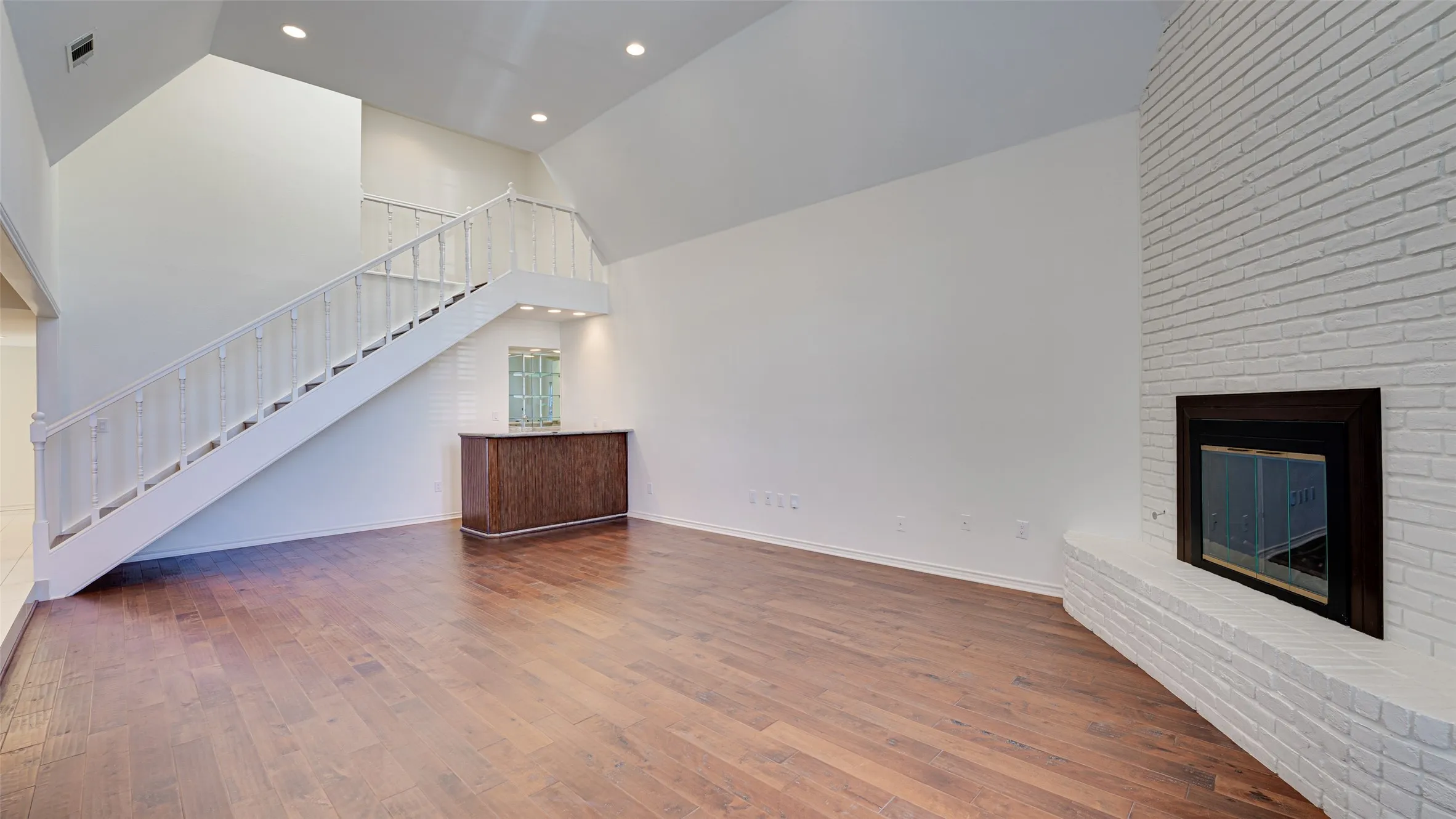Unfurnished living room featuring a brick fireplace, wet bar, hardwood / wood-style flooring, and high vaulted ceiling