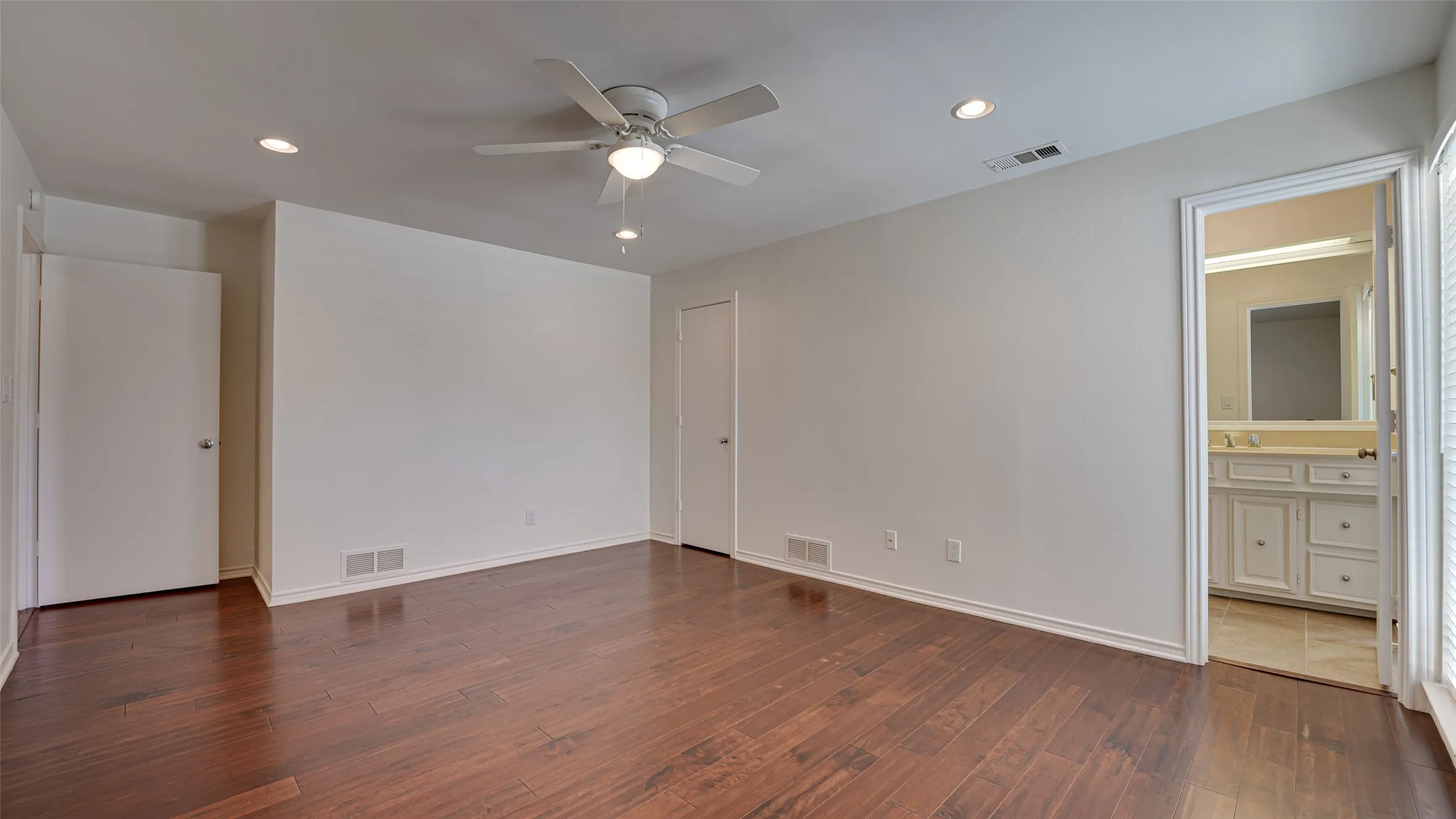 Unfurnished bedroom with connected bathroom, hardwood / wood-style flooring, and ceiling fan