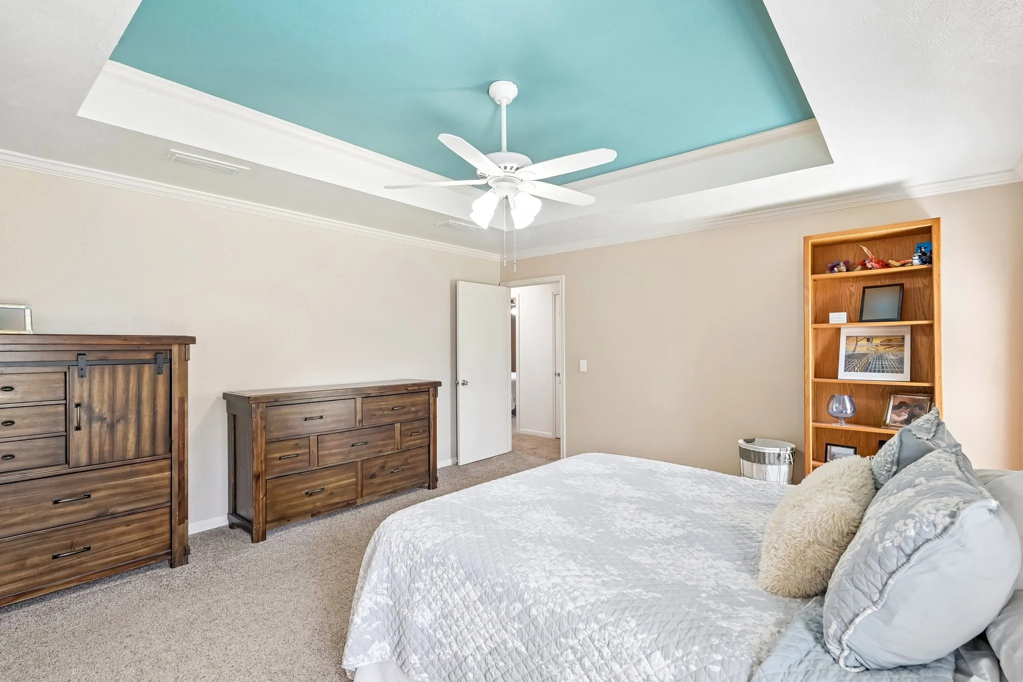Tray ceiling with accent color, crown molding, ceiling fan, and carpeted flooring