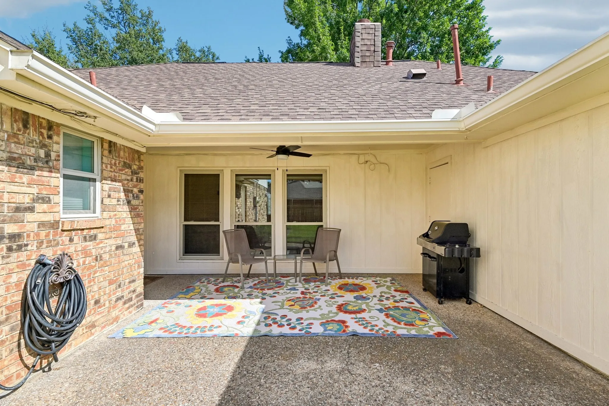 Covered patio featuring an outdoor ceiling fan, brick exterior, and a shingle roof