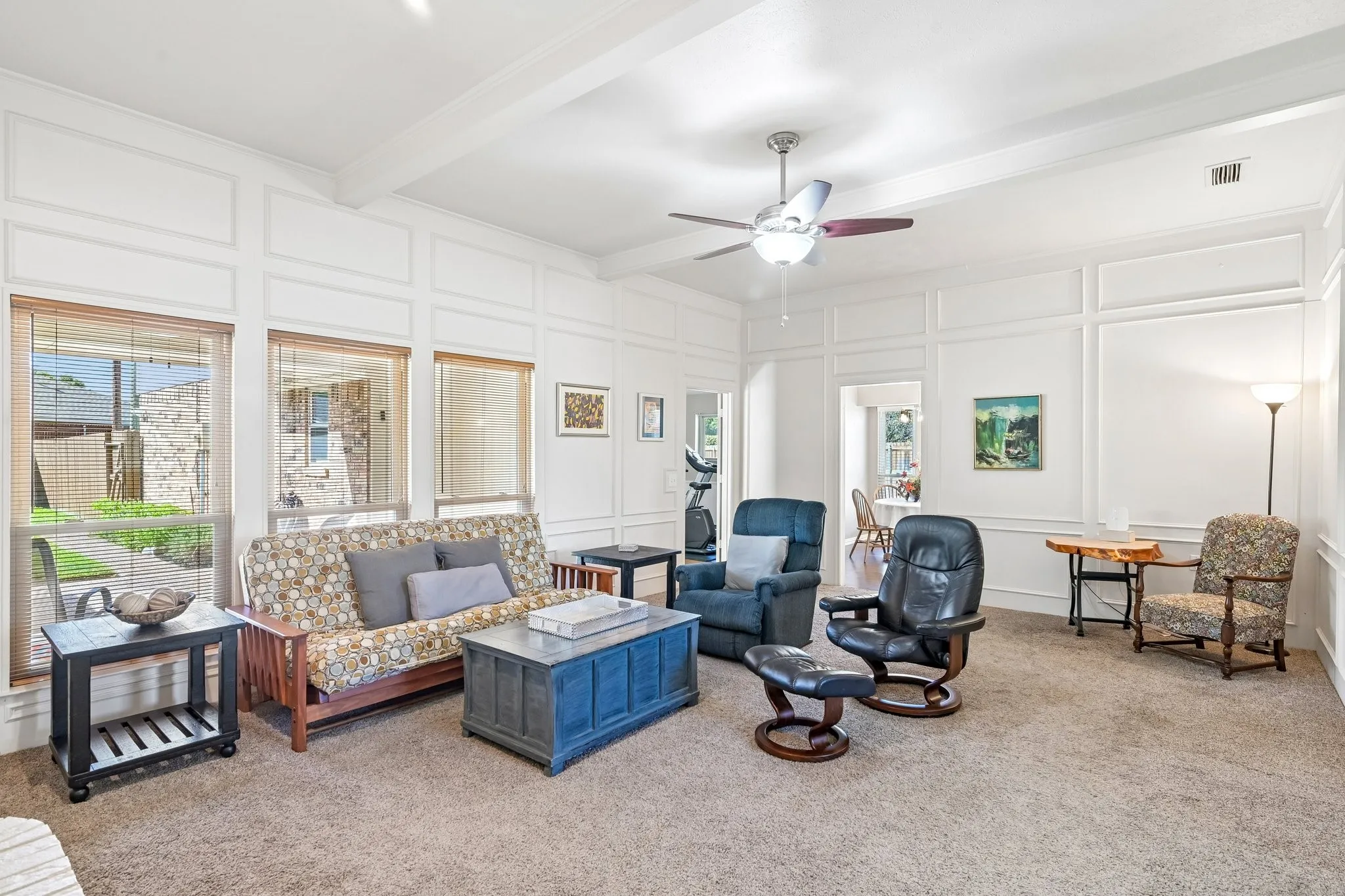 Expansive living space featuring wall paneling, a ceiling fan, carpet flooring, and multiple windows