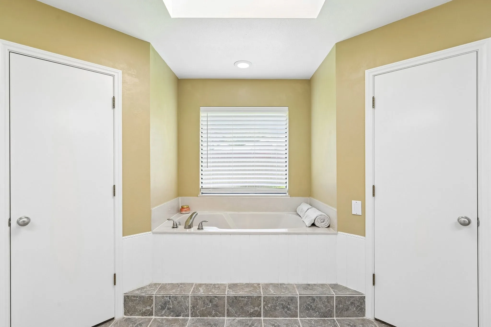 Recessed tub with tile surround, raised tile flooring, and overhead skylight