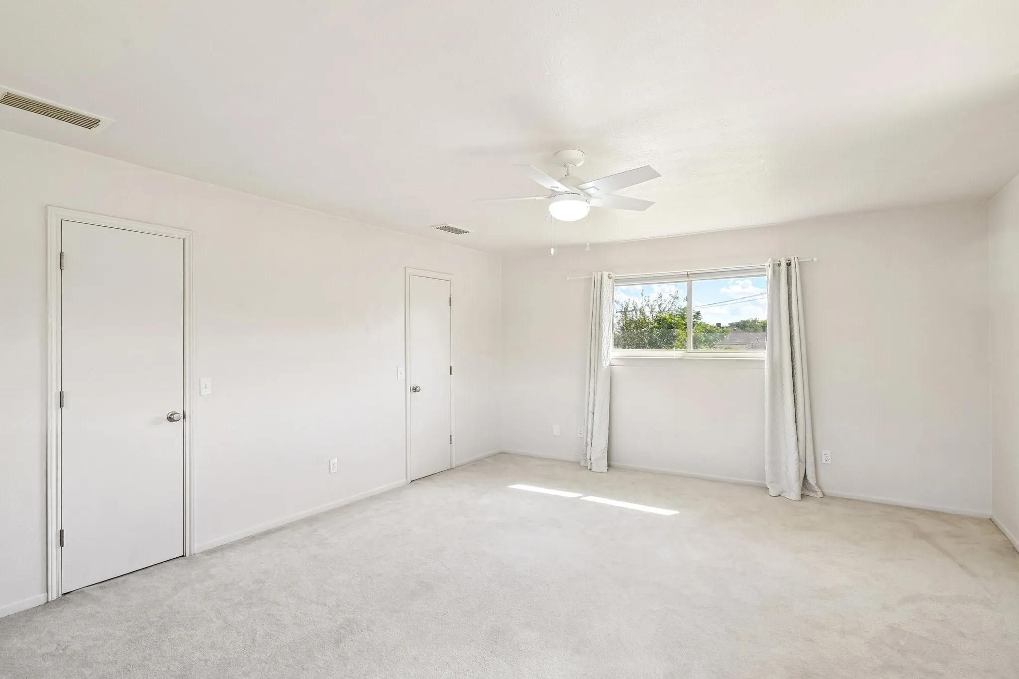 Expansive room with neutral carpeting, white walls, a ceiling fan with integrated lighting, and multiple doors