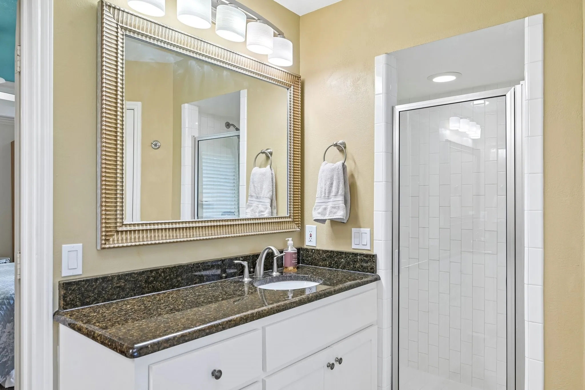 White vanity with dark stone countertop, undermount sink, and chrome faucet
