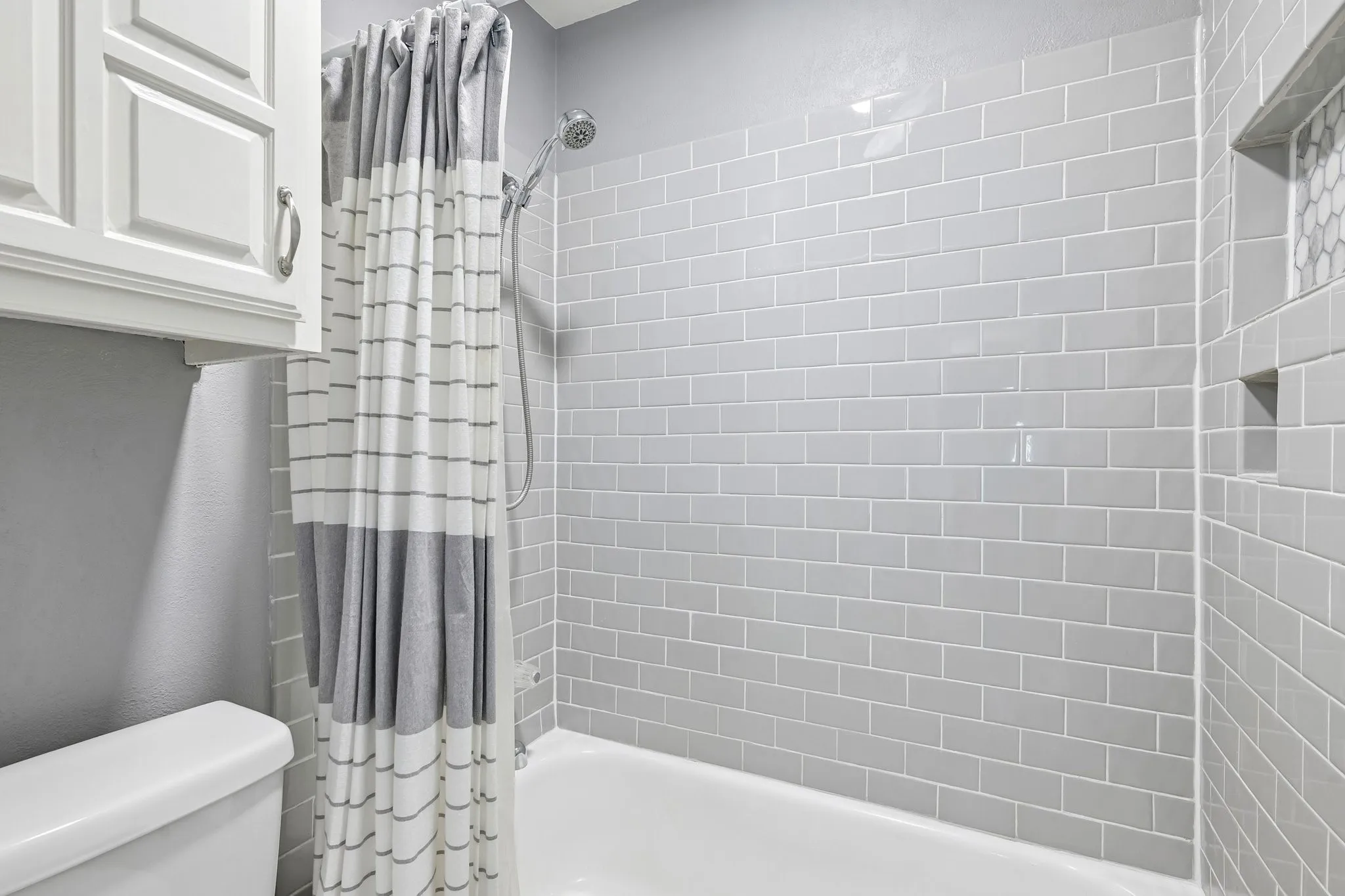 Recessed shower niche with hexagonal tile accent, subway tile surround, white porcelain tub, and chrome showerhead