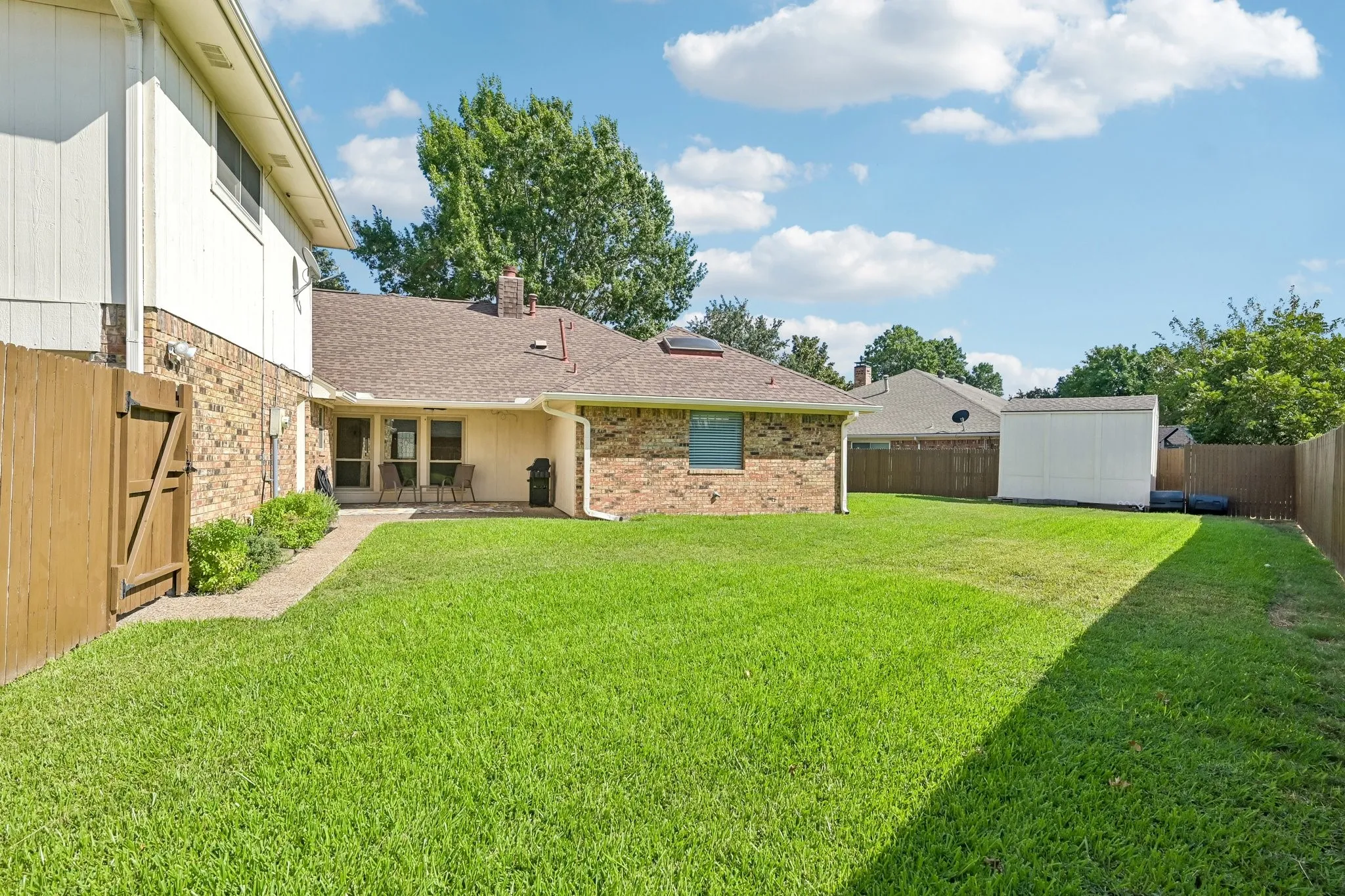 Expansive backyard featuring a manicured lawn, wood fencing, and a detached storage shed