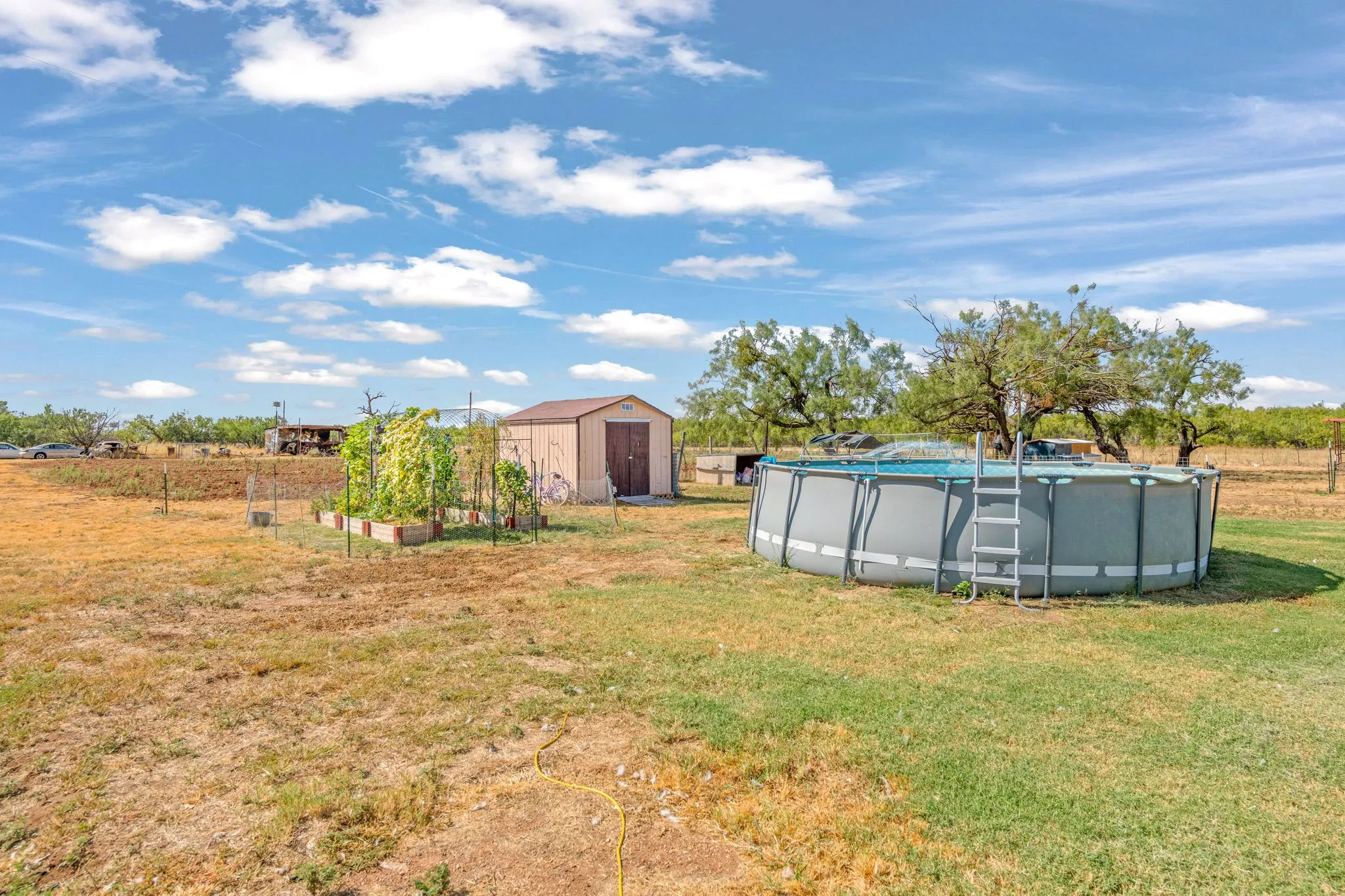 Above ground pool, storage shed, garden beds and trellis