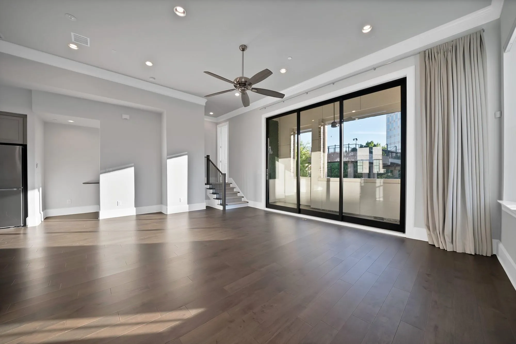 Wide-plank wood-finish flooring, recessed ceiling lighting, a ceiling fan, and black-framed sliding glass doors