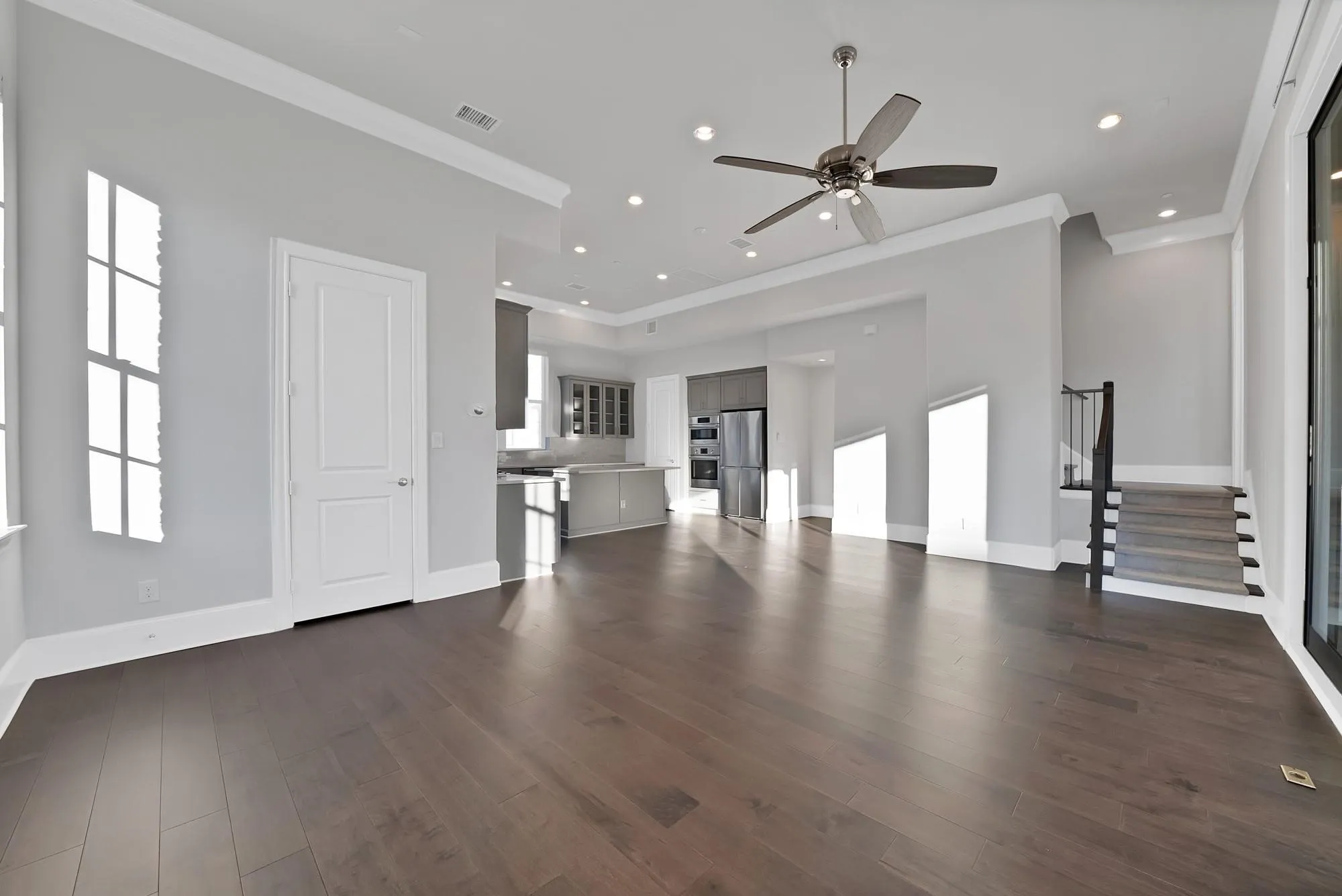 Hardwood-finish flooring, recessed lighting, ceiling fan, crown molding, and a staircase with a black metal railing