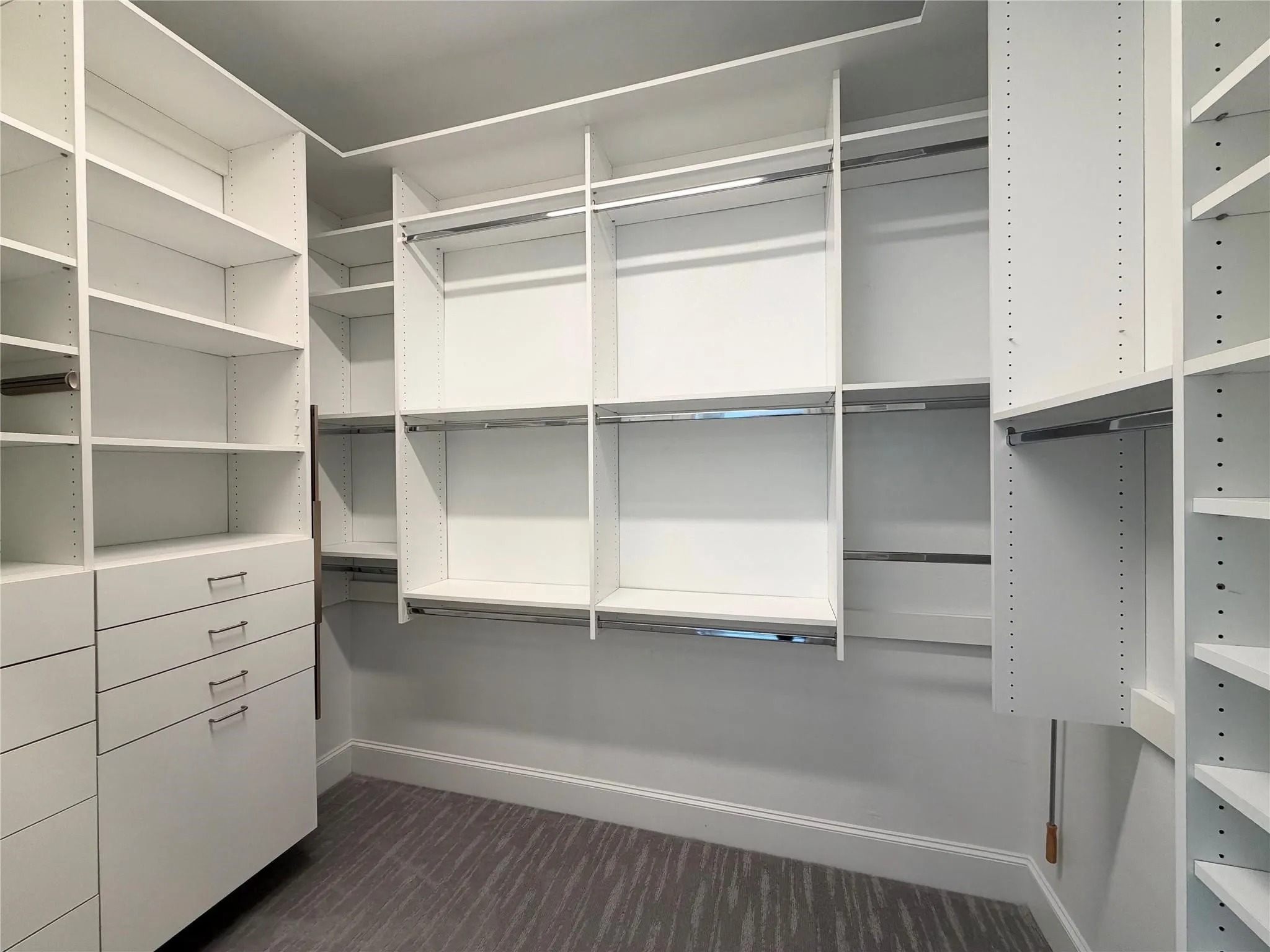 Custom built-in closet system with multiple shelving units, integrated drawers, hanging rods, and a patterned carpet