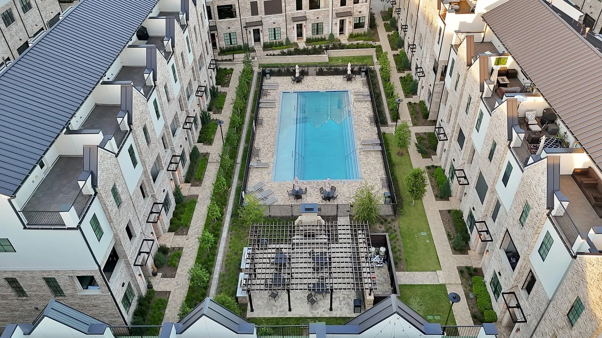 Central rectangular swimming pool, structured landscaping, paved walkways, and a covered outdoor seating area