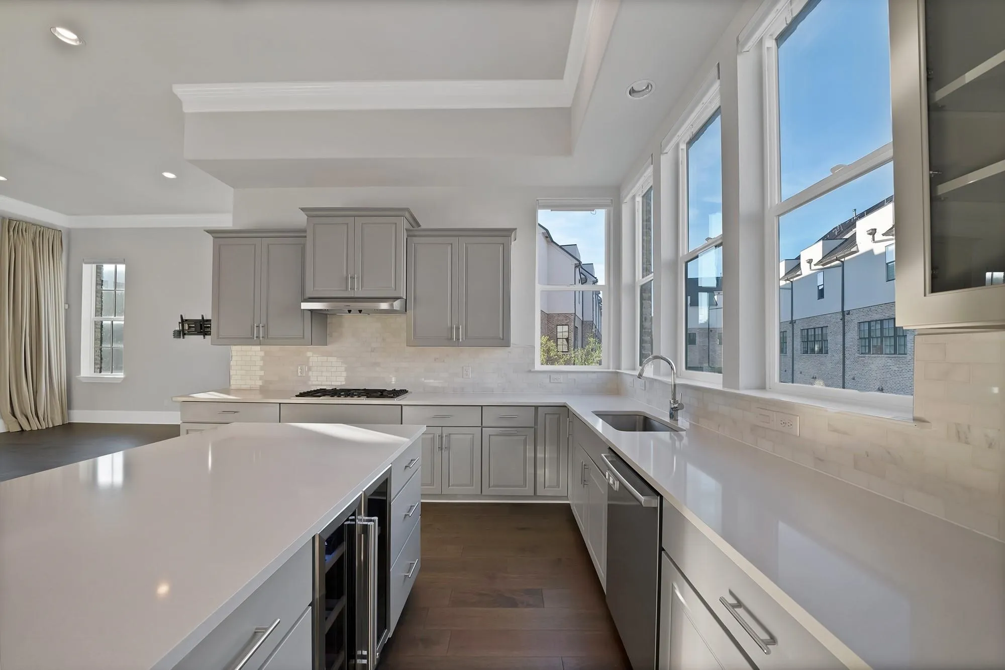 Contemporary kitchen featuring gray cabinetry, light-toned countertops, a full suite of stainless steel appliances, and a beverage cooler