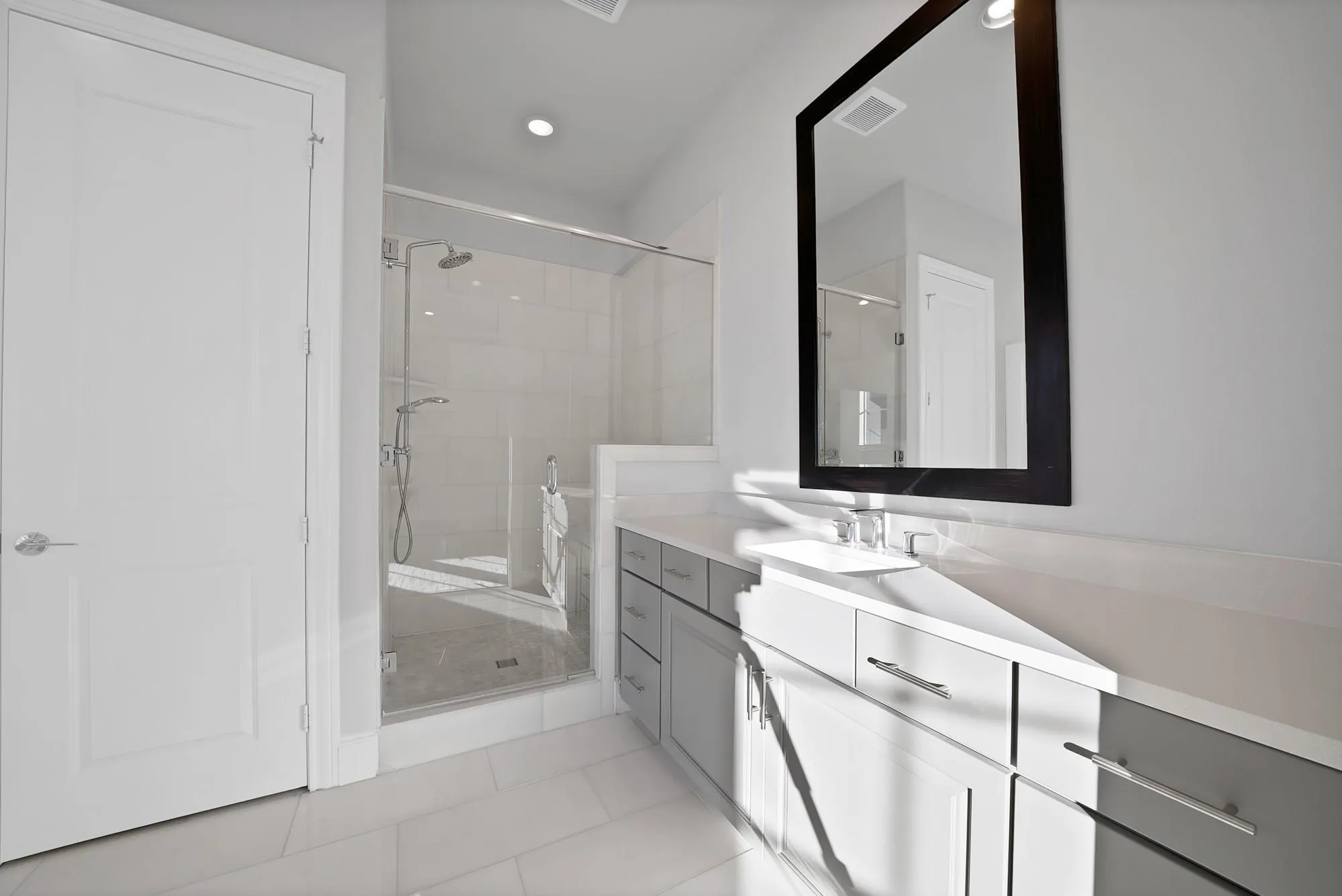 Full-height tiled shower with glass enclosure, dual shower heads, double vanity with white countertops, and contemporary gray cabinetry