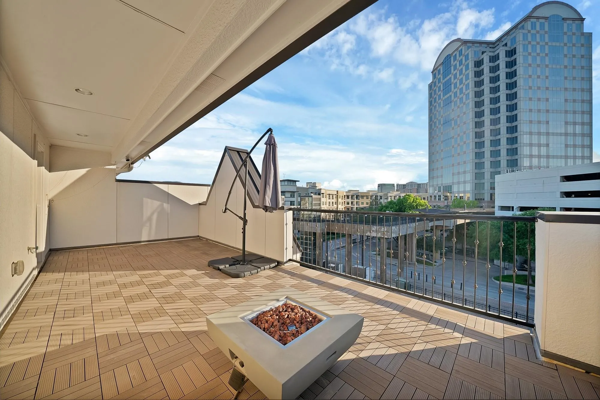 Expansive balcony featuring wood-finish tile flooring, a gas fire pit, and a black wrought iron railing